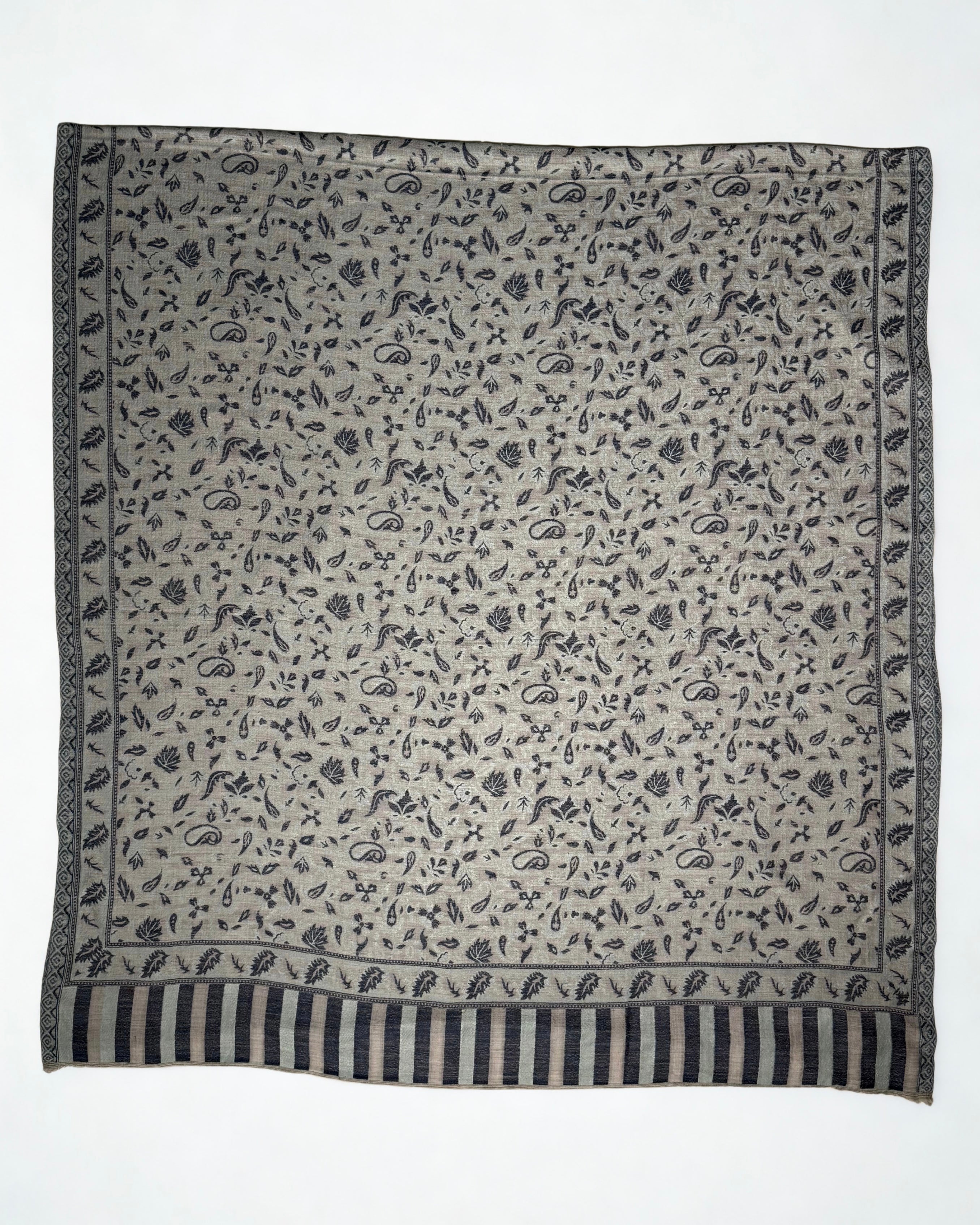 Close view of the indigo paisley motifs, leaf border and striped end panel on a stone grey pashmina shawl