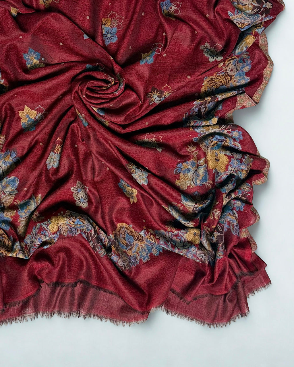 Close view of the naturalistic blue and gold roses woven into the border of a claret pashmina Kani shawl