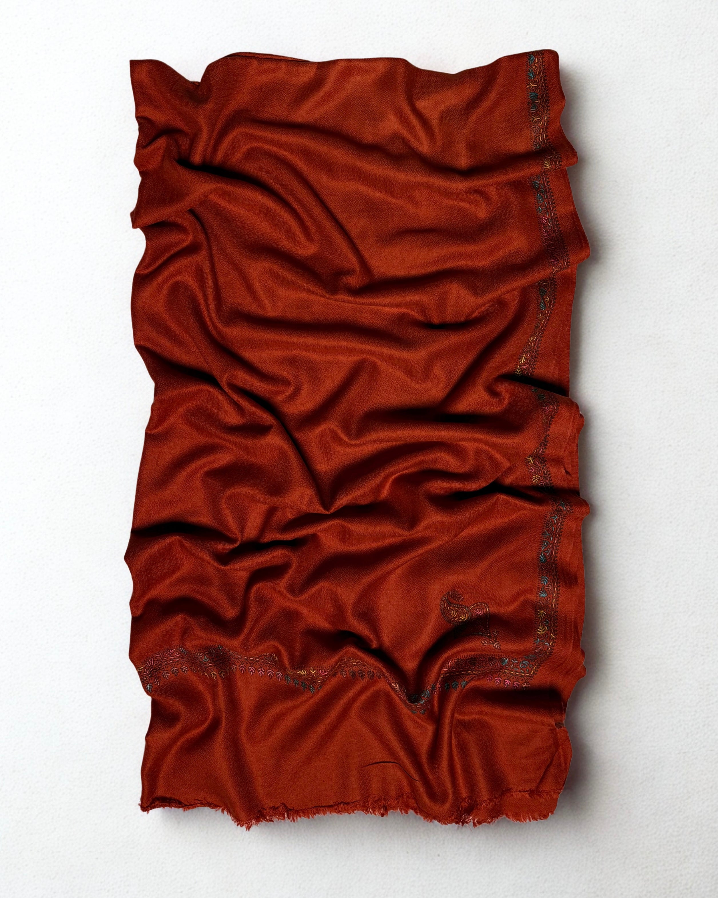 Close view of the teal, rose and ochre hand embroidery on the border of a rust Swati Shahtoosh shawl