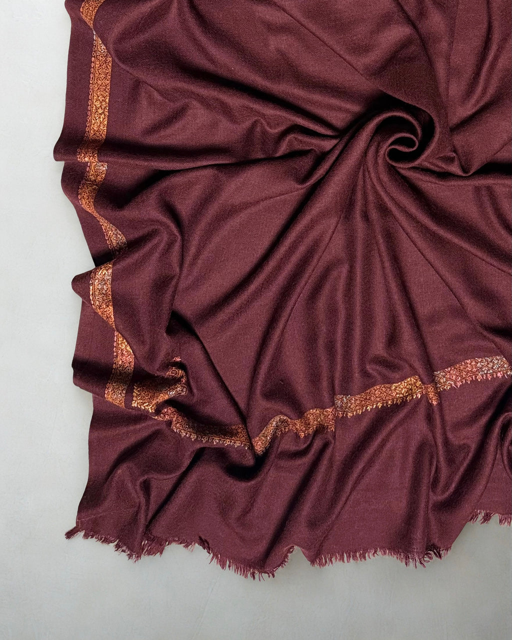Deep maroon Swati Shahtoosh shawl folded to show both embroidered corner buta and the fringed edge