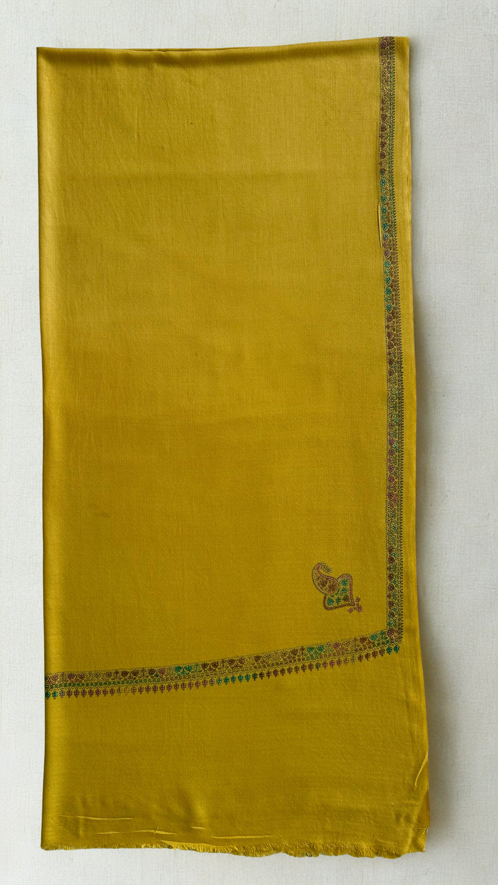 Mustard gold Swati Shahtoosh shawl folded flat, showing the narrow embroidered border and corner buta