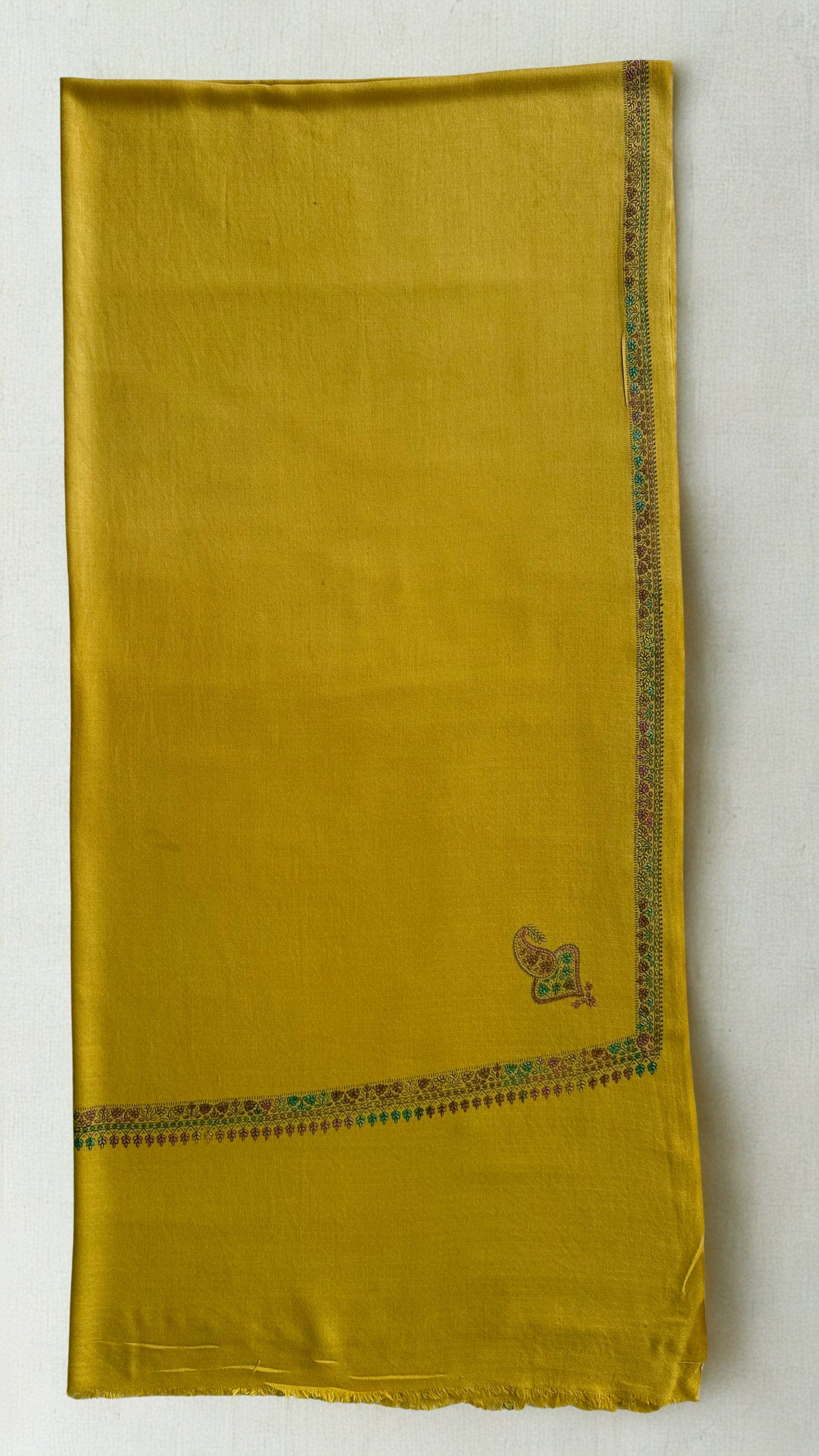 Mustard gold Swati Shahtoosh shawl folded flat, showing the narrow embroidered border and corner buta