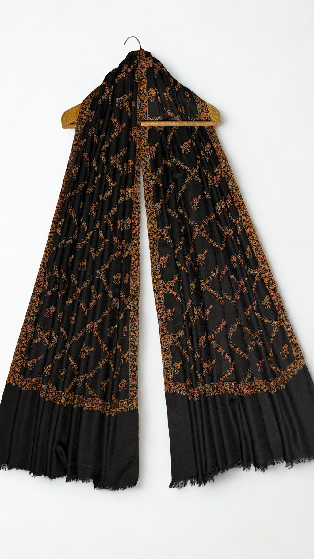 Black Swati Shahtoosh shawl draped over a wooden hanger, gold jaal embroidery running through the folds