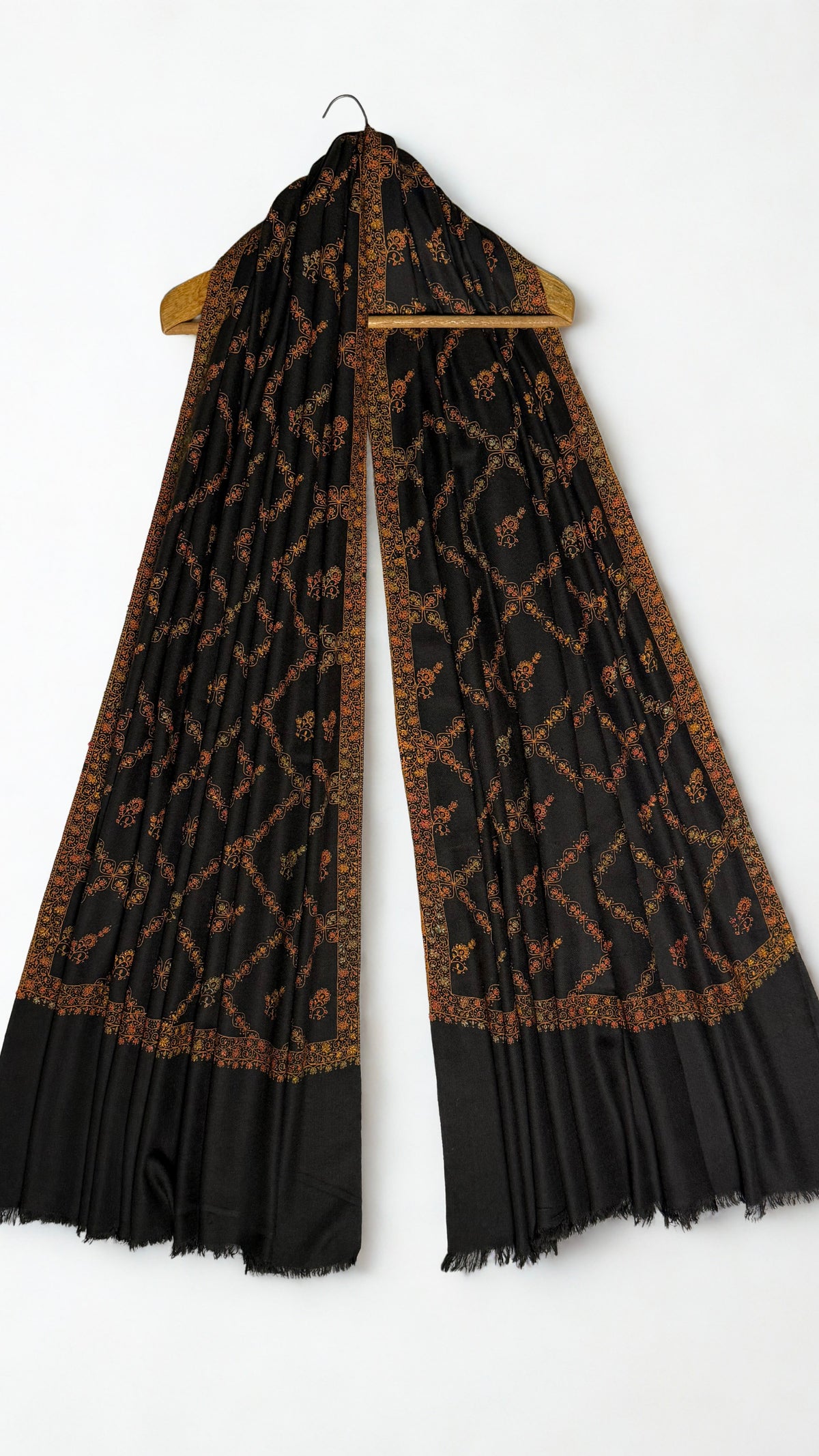 Black Swati Shahtoosh shawl draped over a wooden hanger, gold jaal embroidery running through the folds