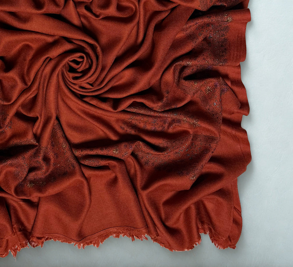 Close view of the rust Swati Shahtoosh shawl gathered in folds, showing the fine self-coloured lattice weave against the embroidered border