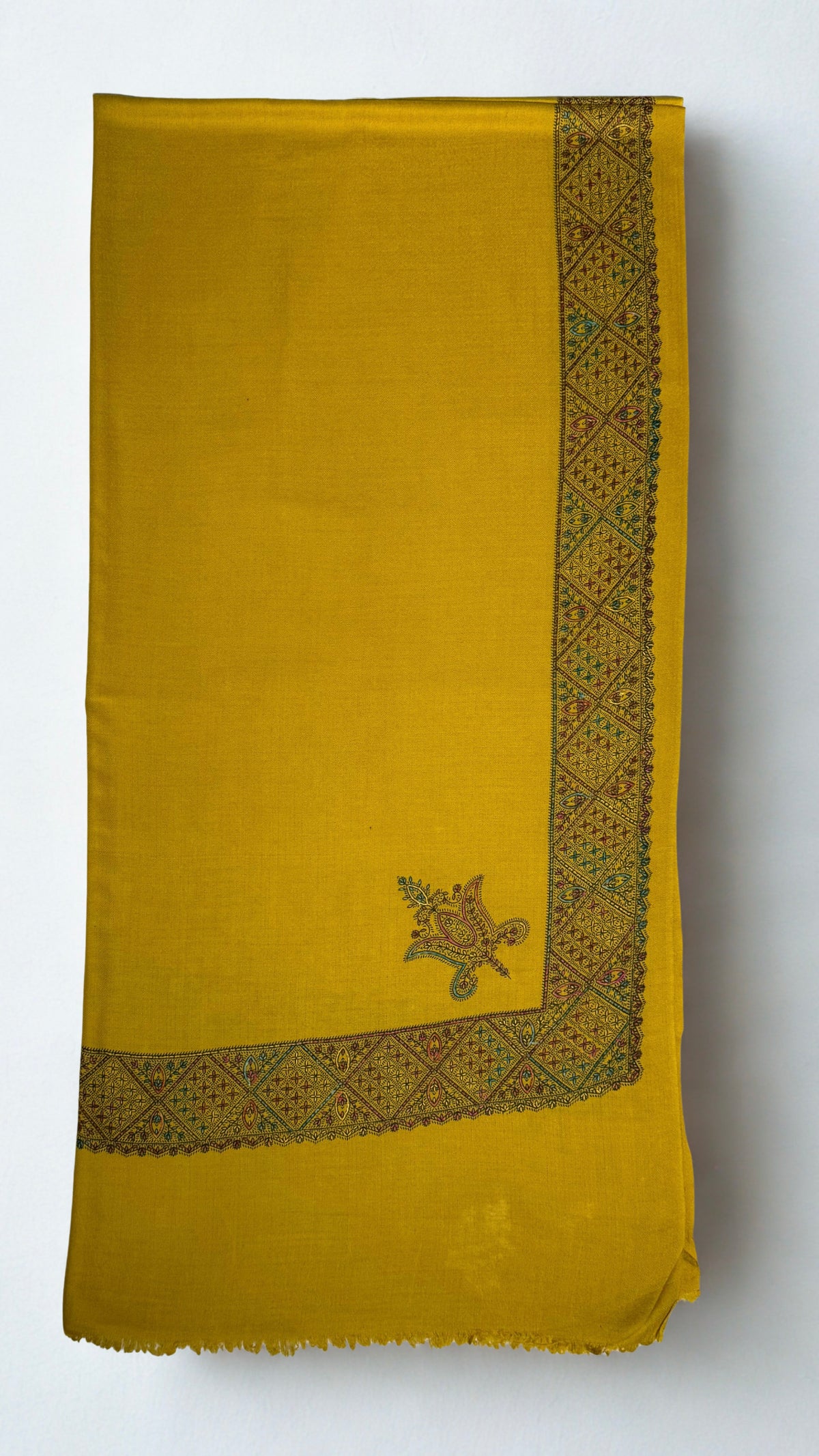 Mustard gold Swati Shahtoosh shawl folded flat, the wide hand-embroidered lattice border running down one edge with a paisley buta on the field