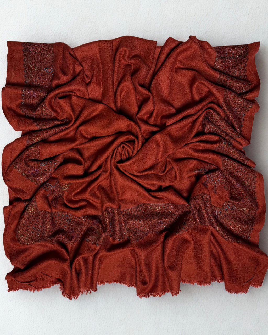 Full view of the rust Swati Shahtoosh shawl gathered in a swirl, the hand-embroidered lattice border framing all four sides