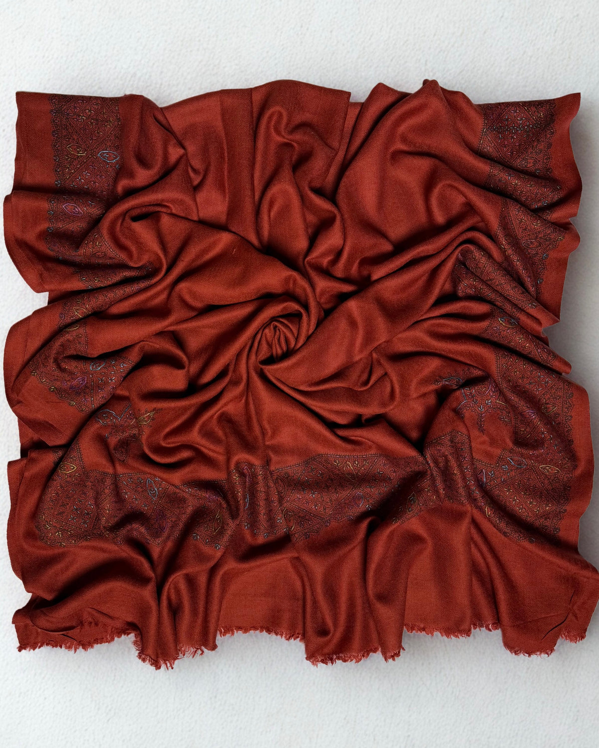 Full view of the rust Swati Shahtoosh shawl gathered in a swirl, the hand-embroidered lattice border framing all four sides