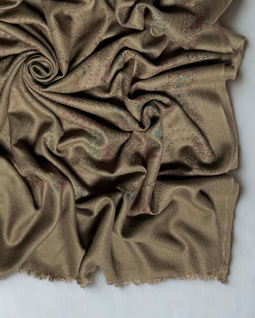 Close view of the olive brown Swati Shahtoosh shawl in folds, the fine outlined paisleys and small rose and teal flowerheads against the self-coloured herringbone