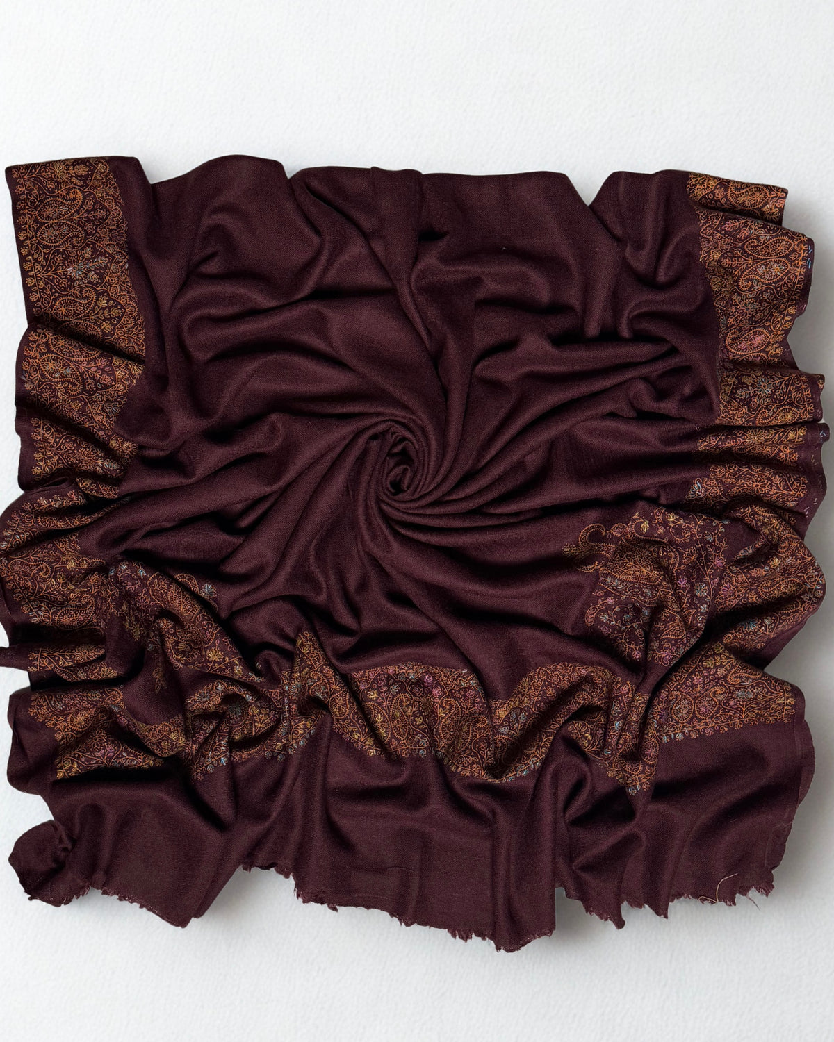 Deep maroon Swati Shahtoosh shawl gathered in a swirl, the wide hand-embroidered paisley border framing all four sides