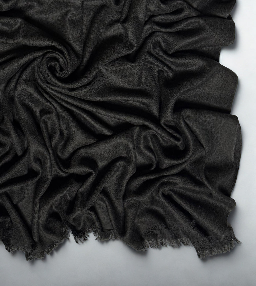 Close view of the charcoal black Swati Shahtoosh shawl in folds, showing the diamond weave texture and fringed edge