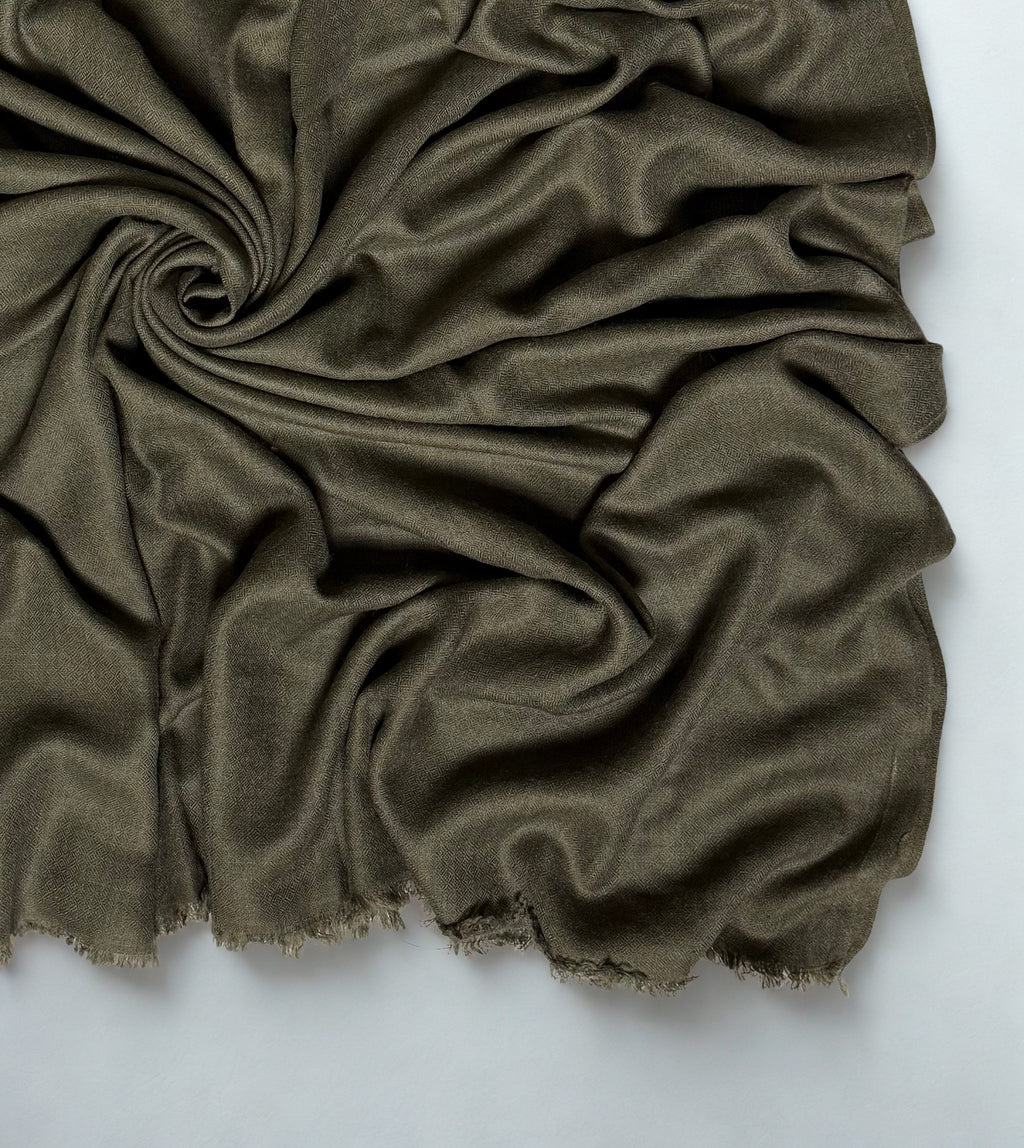 Close view of the olive Swati Shahtoosh shawl in folds, showing the diamond weave texture and fringed edge