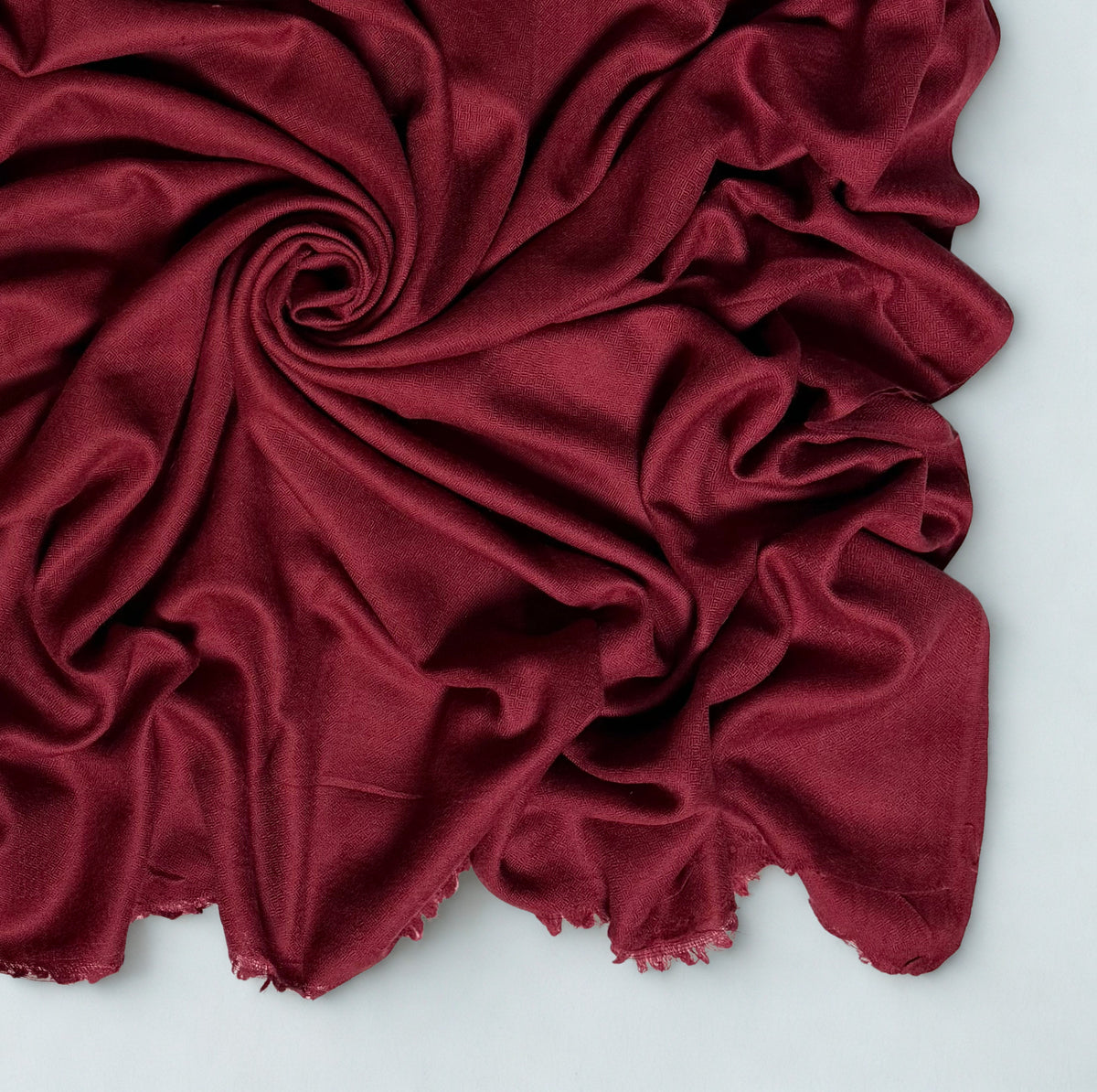 Close view of the maroon Swati Shahtoosh shawl in folds, showing the diamond weave texture and fringed edge