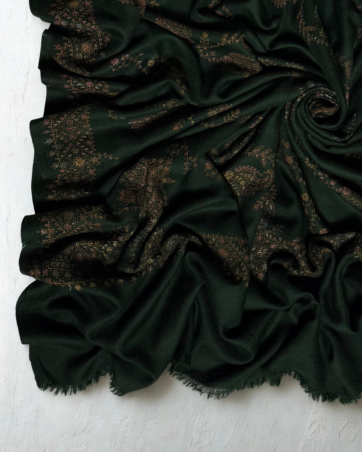 Close-up of a forest green Swati Shahtoosh shawl swirled to show copper and gold hand embroidery and the soft fringed end
