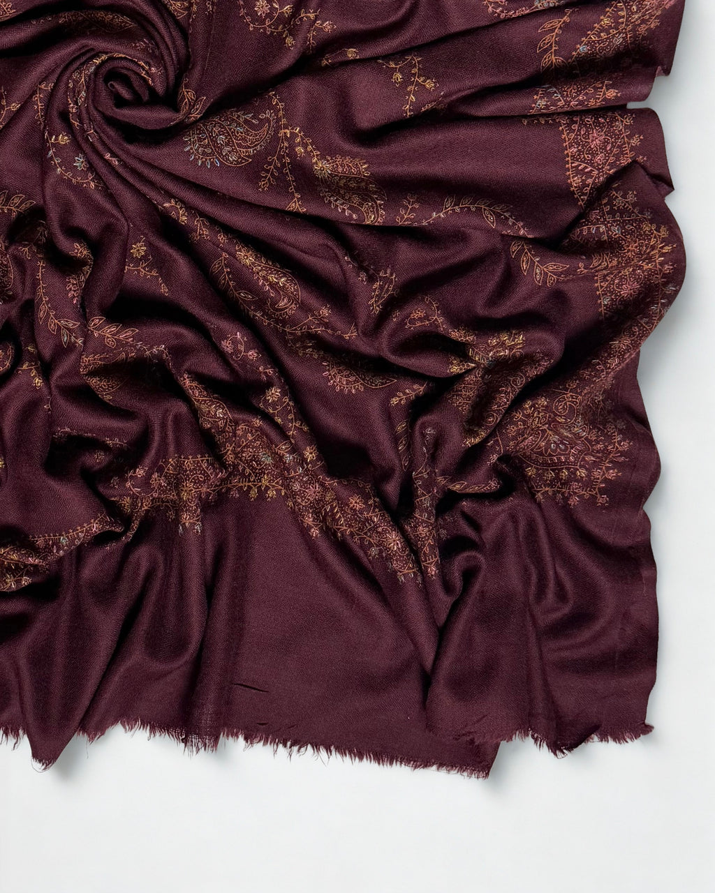 Close-up of a deep maroon Swati Shahtoosh shawl swirled to show copper and gold hand embroidery and the soft fringed end