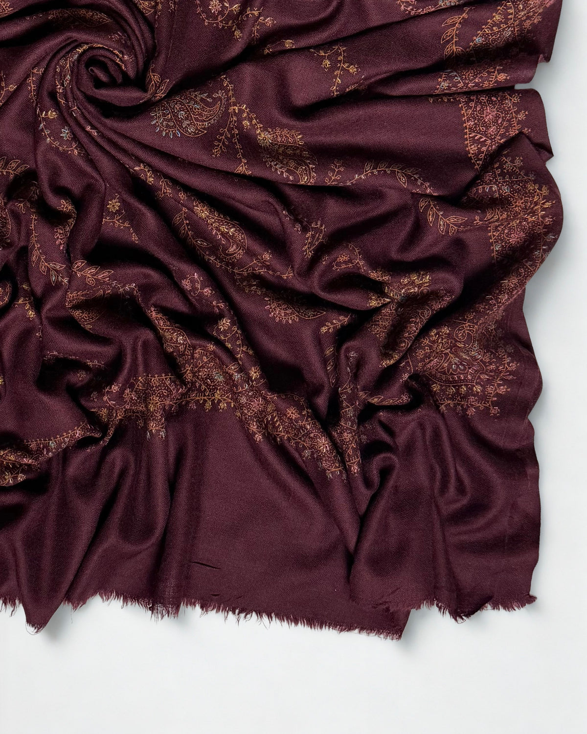 Close-up of a deep maroon Swati Shahtoosh shawl swirled to show copper and gold hand embroidery and the soft fringed end