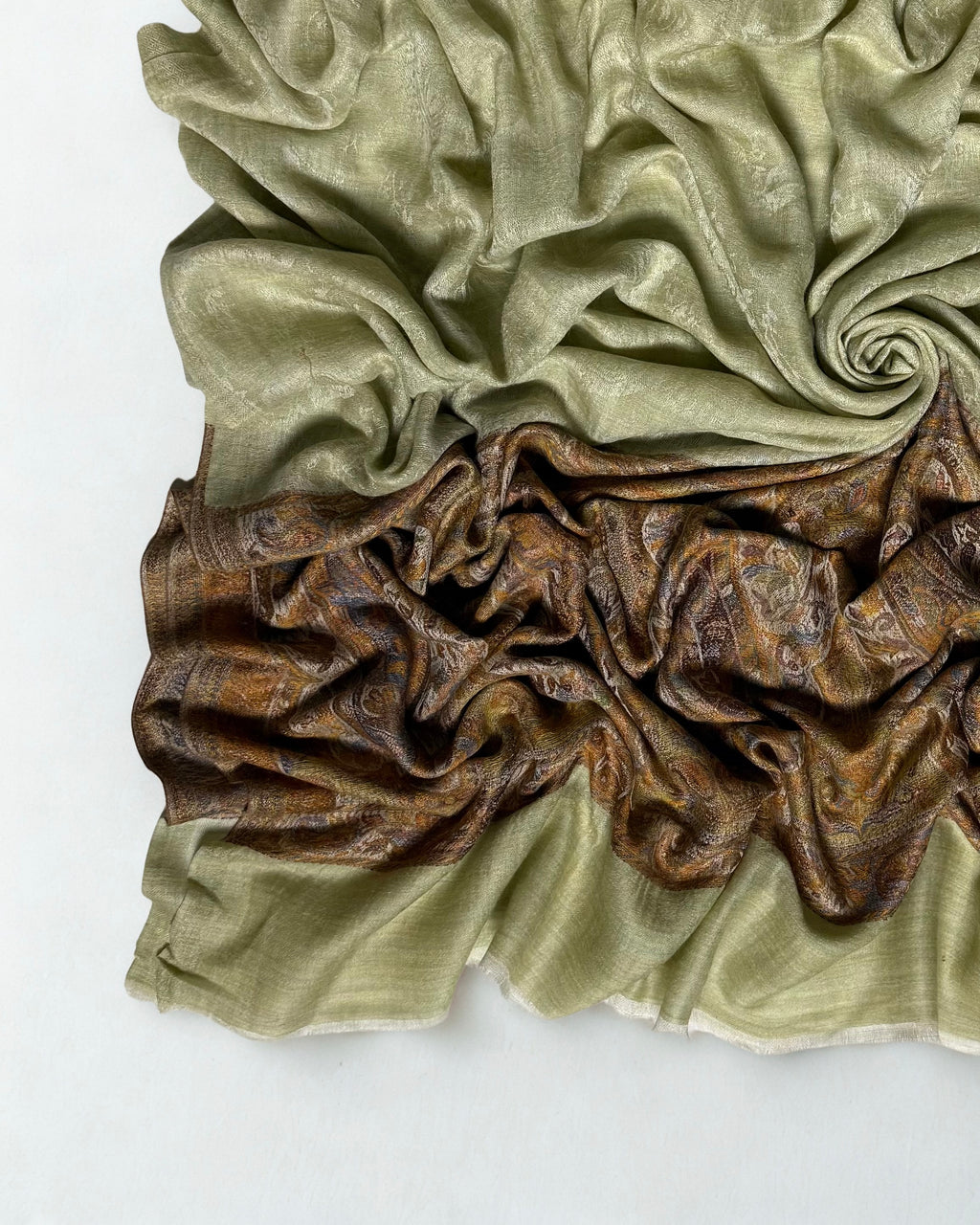 Close-up of a pistachio Palladar shawl swirled to show the faint woven paisley in the field and the bronze palla