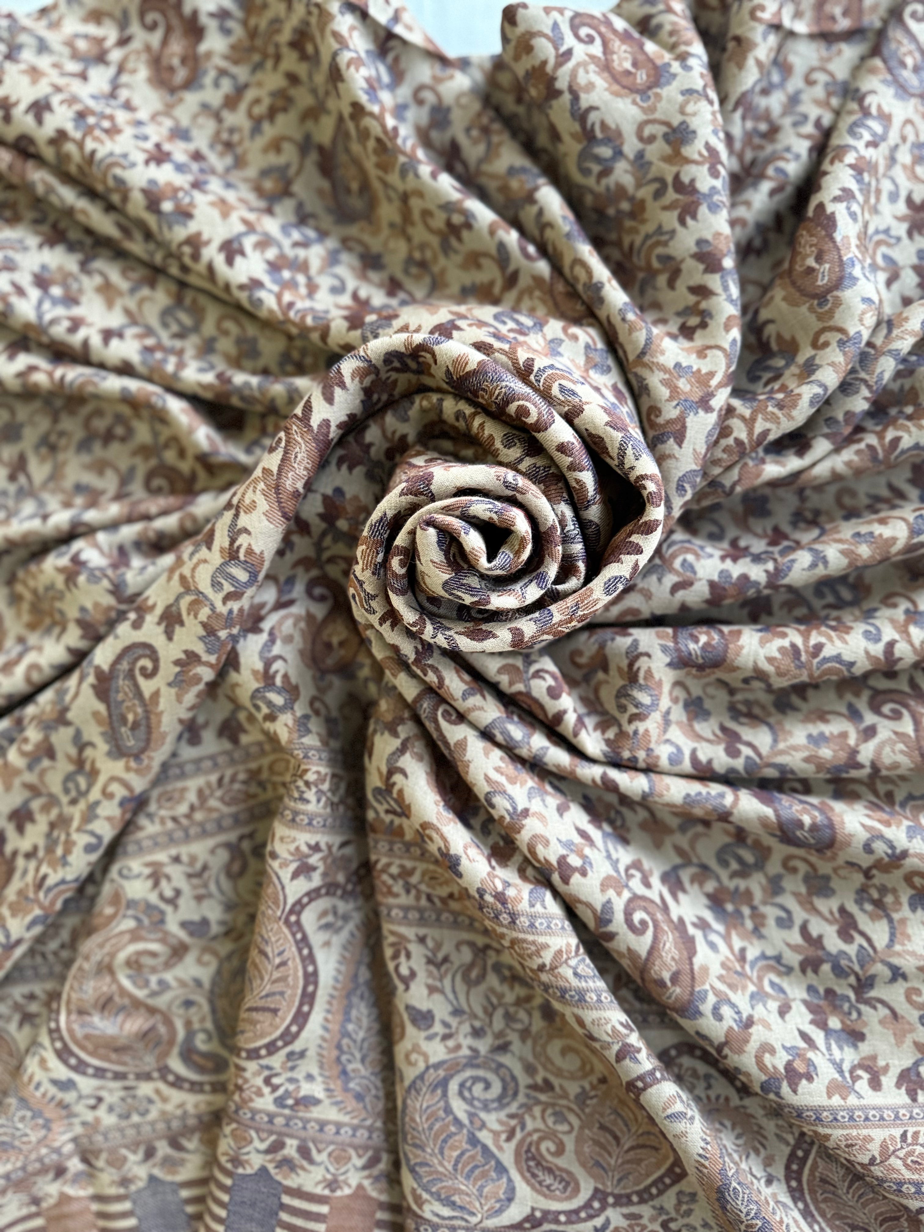 Sand Kani pashmina shawl folded to show the deep woven border of large curling paisleys in indigo and chestnut