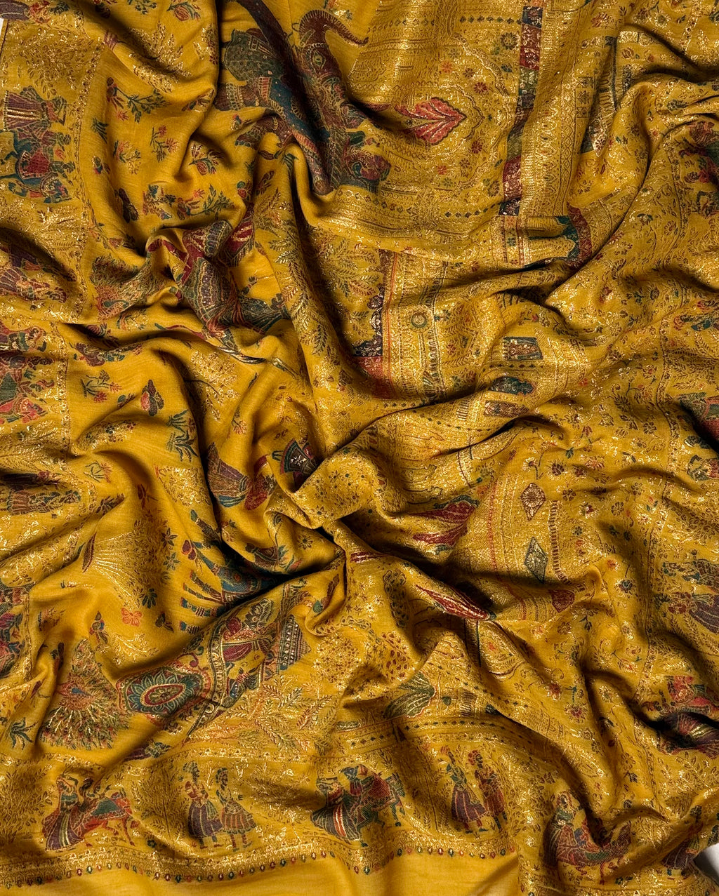 Full length of the mustard Mughal court Kani pashmina shawl laid flat, procession field framed by a border of standing figures