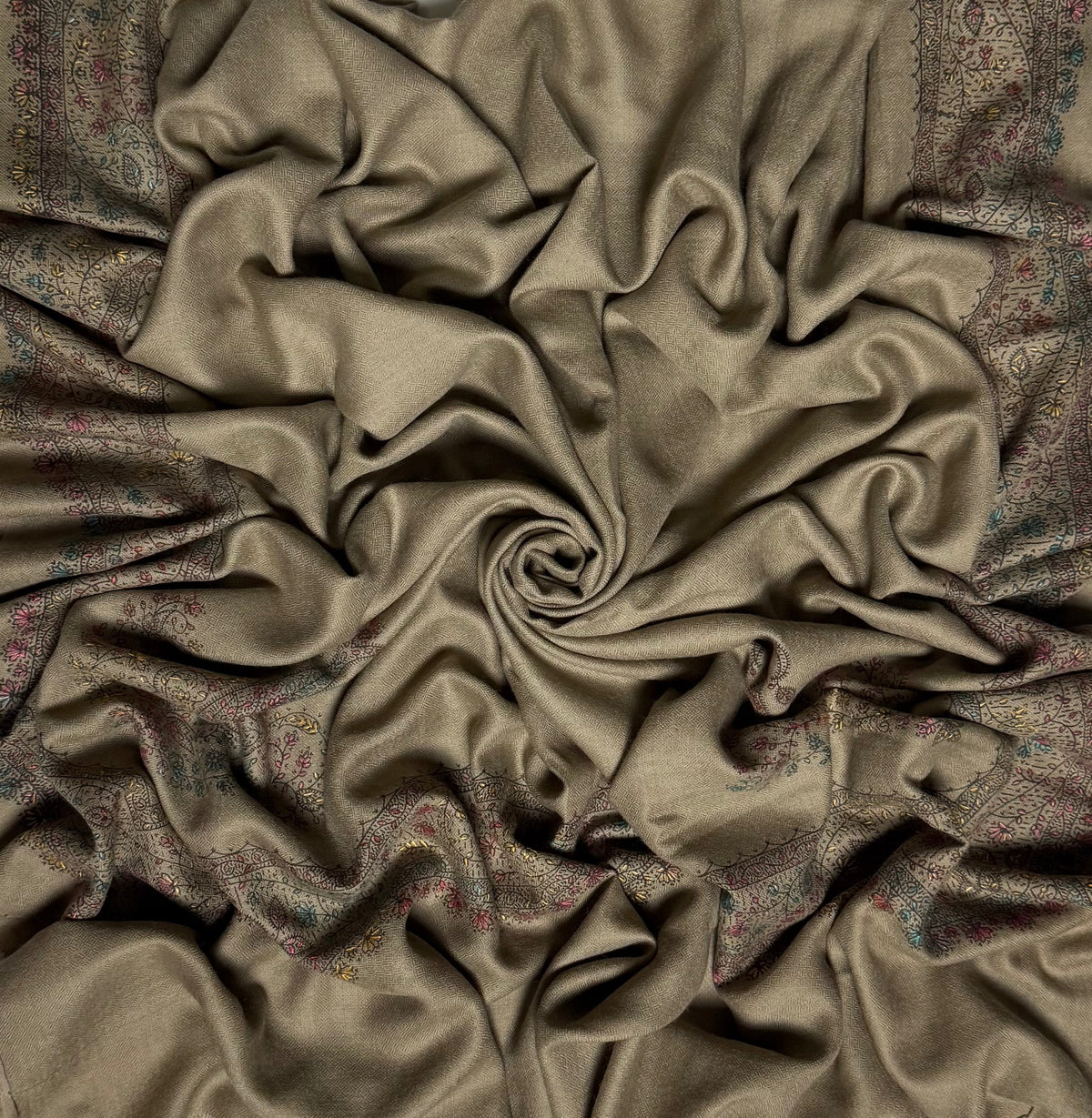 Close view of the grey Swati Shahtoosh shawl, showing the hand-embroidered floral vine border in faded teal, rose and citron against the self-coloured herringbone weave