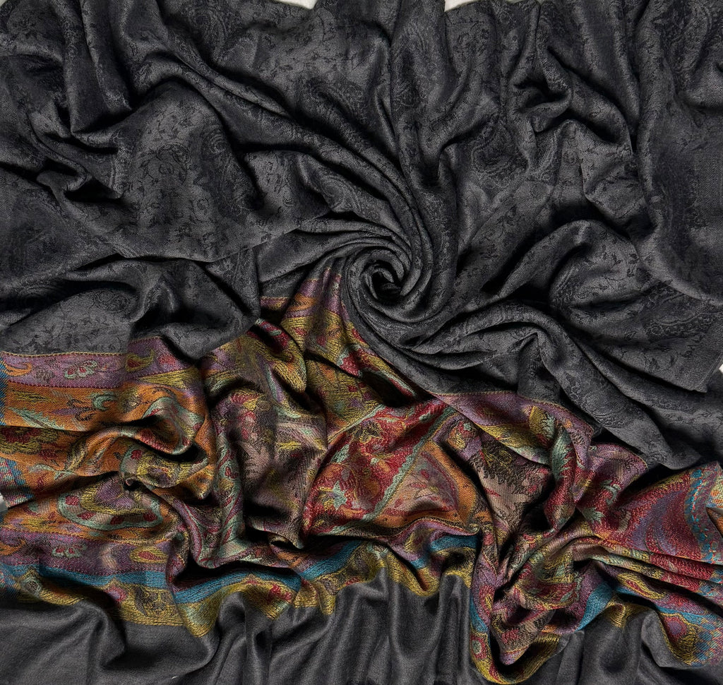Close-up of a dark charcoal Palladar shawl swirled to show the sheen of the pashmina and the saffron and crimson paisley end