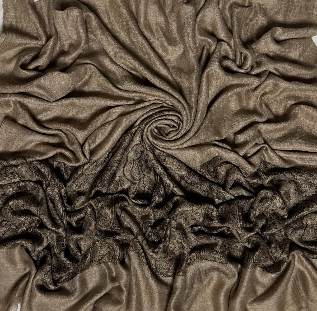 Fawn pashmina ring shawl swirled to show the sheen of the fine pashmina and the woven black paisley end