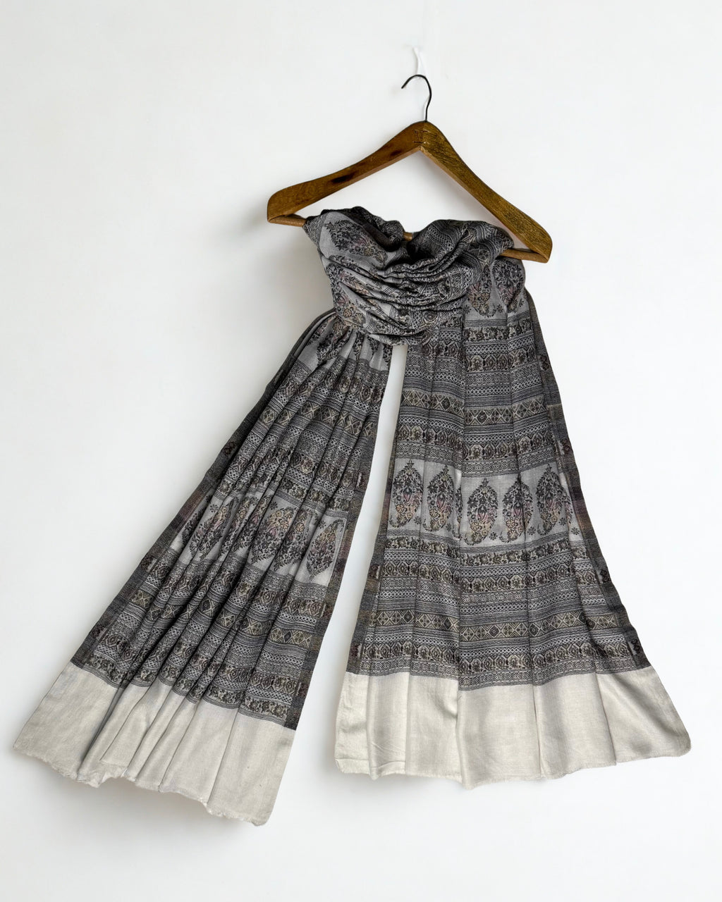 Silver grey Indian pashmina shawl on a wooden hanger, falling in fine pleats to show its full length and ivory end panels