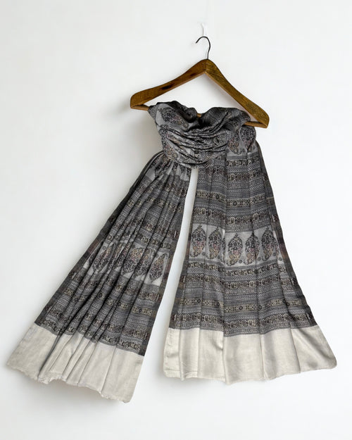 Silver grey Indian pashmina shawl on a wooden hanger, falling in fine pleats to show its full length and ivory end panels