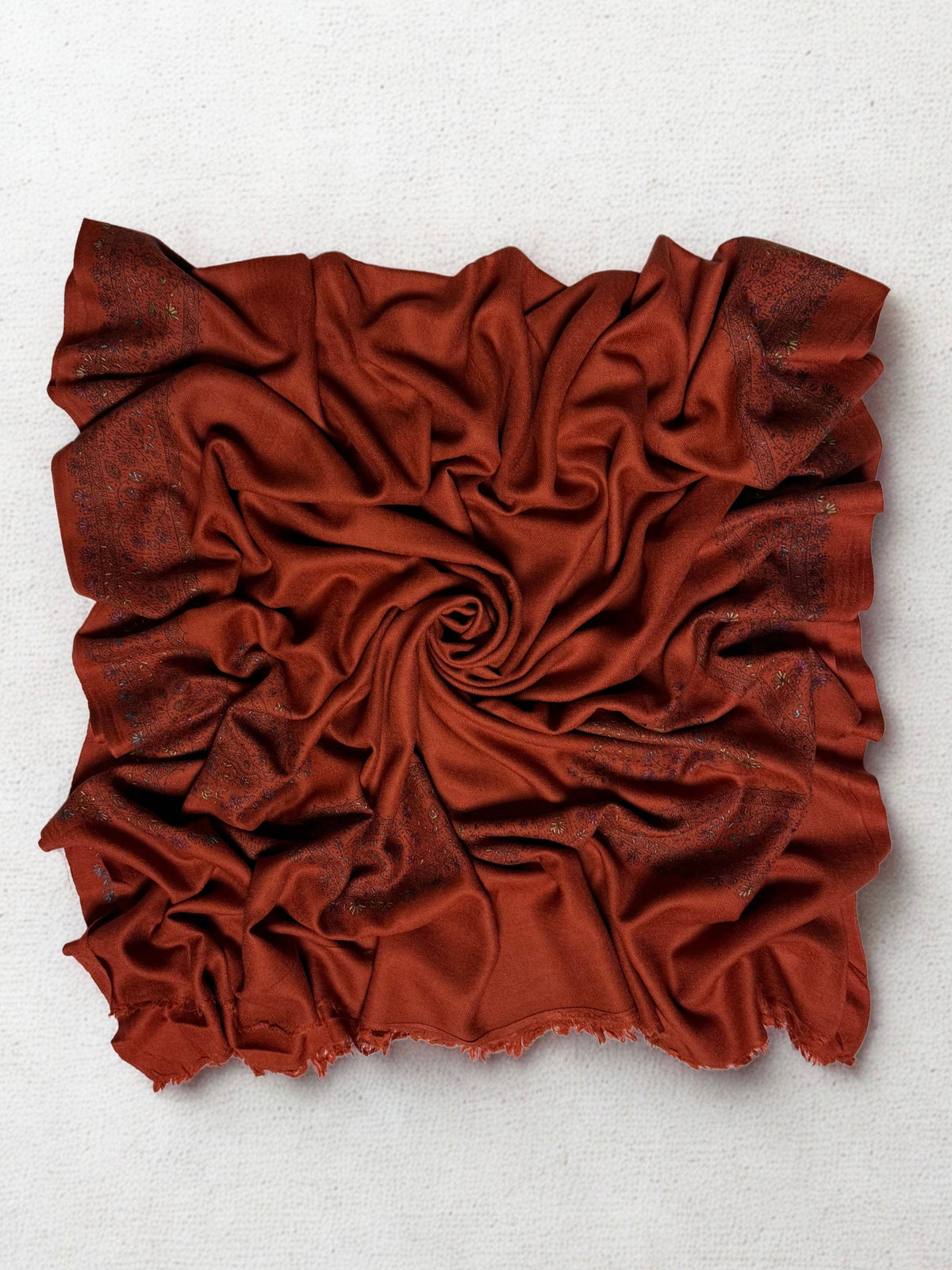 Full view of the rust Swati Shahtoosh shawl gathered in a swirl, the hand-embroidered vine border framing all four sides