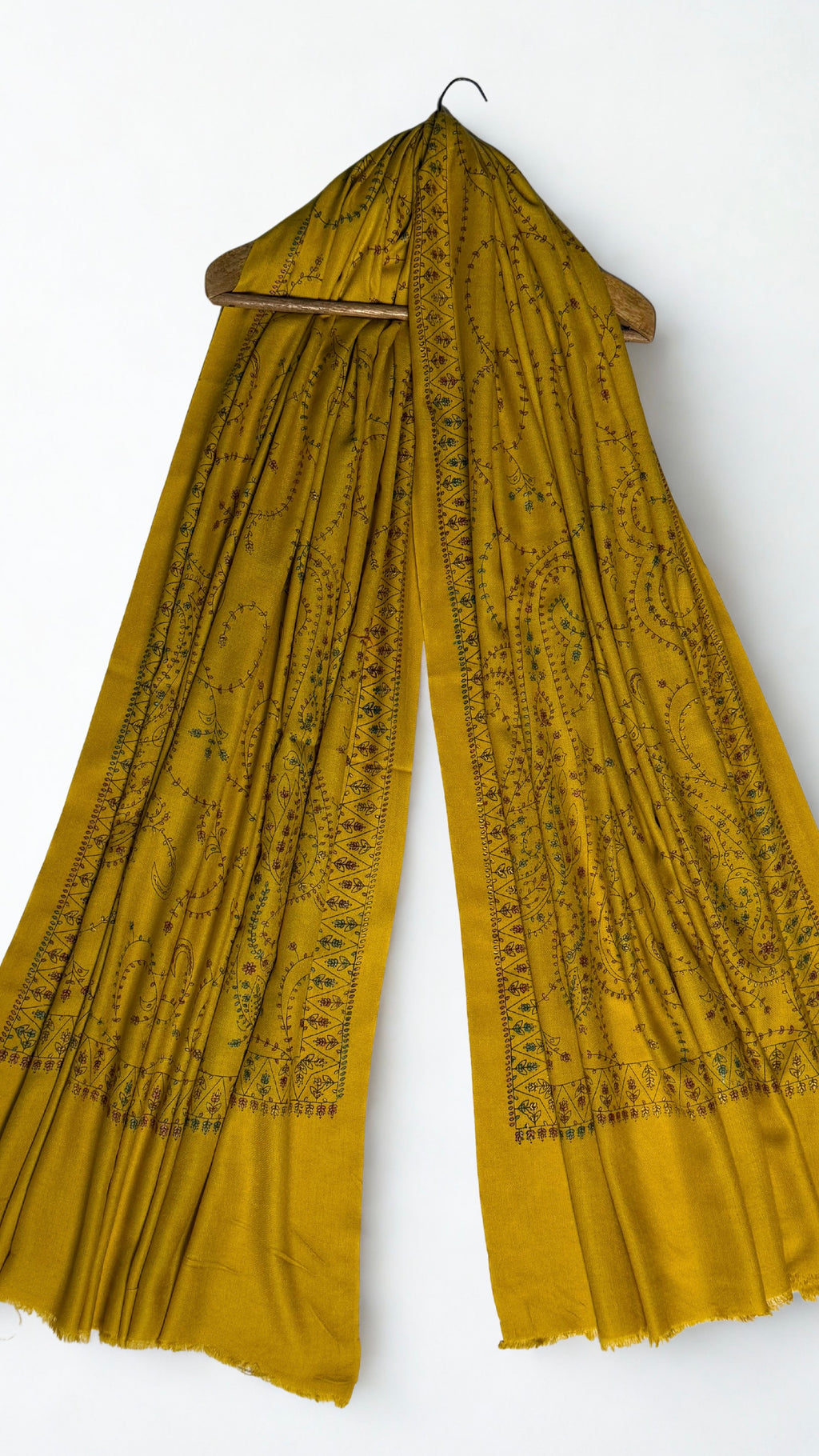 Mustard Swati Shahtoosh shawl draped over a wooden hanger, embroidery running through the folds