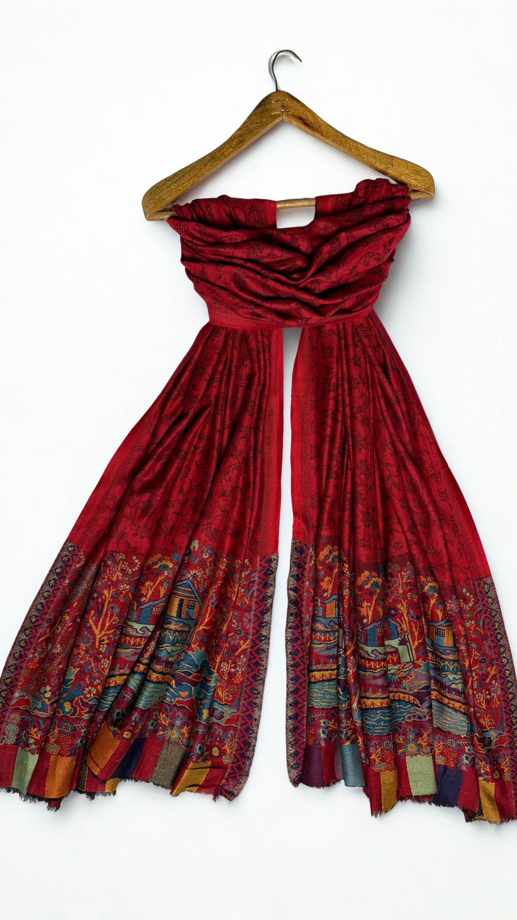 Red pashmina shawl draped on a wooden hanger, both ends showing the landscape borders