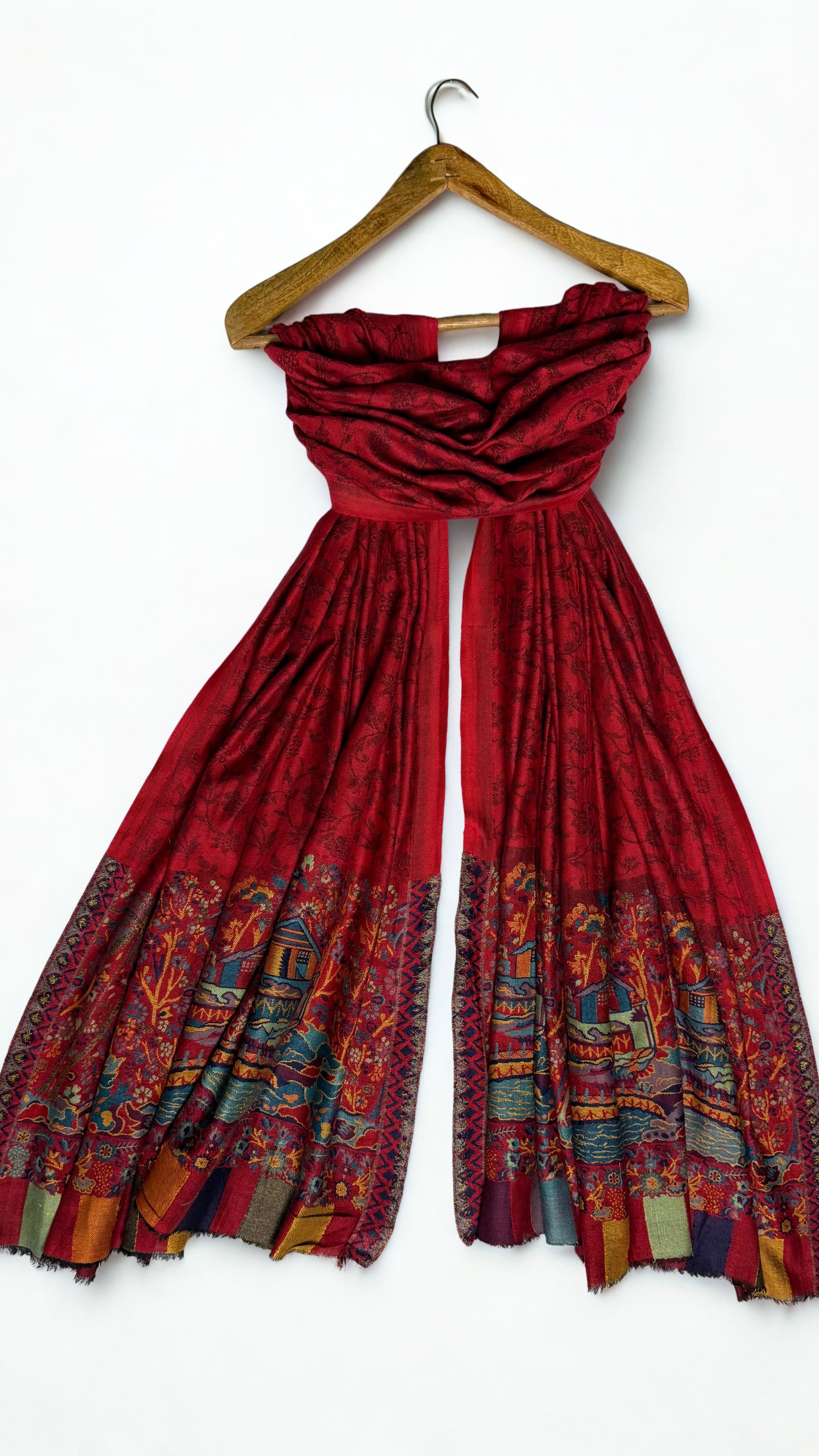 Red pashmina shawl draped on a wooden hanger, both ends showing the landscape borders