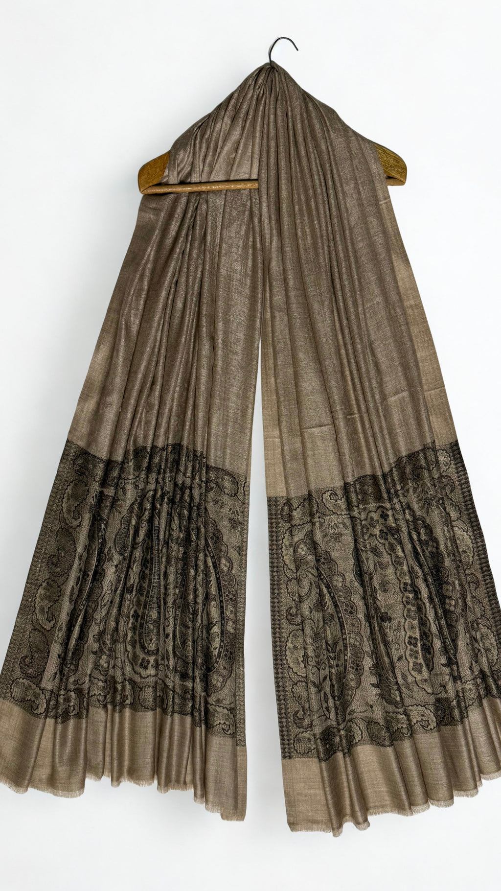 Fawn Palladar shawl hanging from a wooden hanger, with black paisley pallas at both ends
