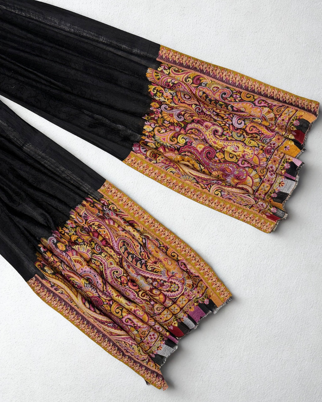 Full length of a black ek rukh pashmina ring shawl on a hanger, plain black body with rose-gold paisley ends
