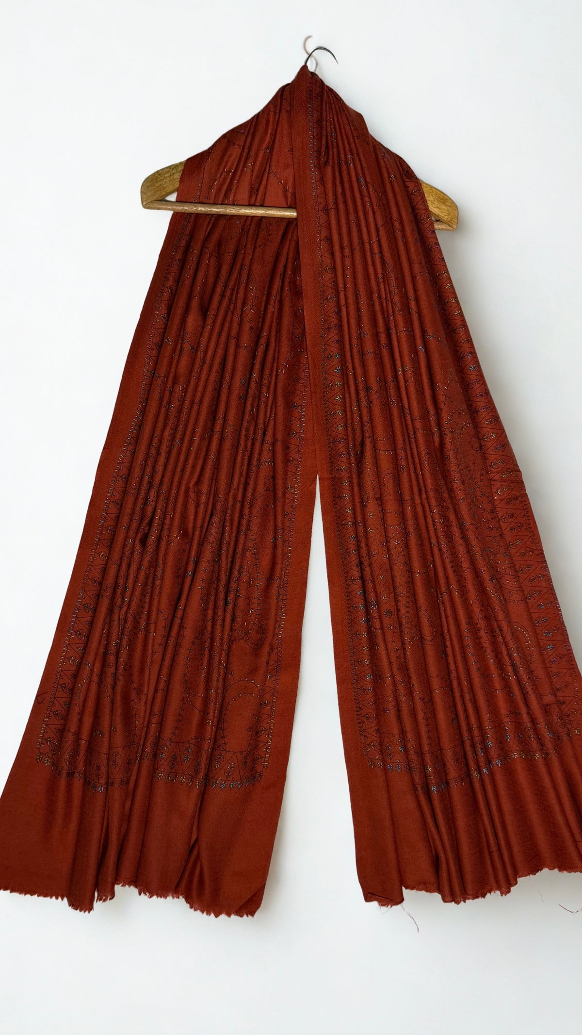 Full-length rust Swati Shahtoosh shawl on a wooden hanger, hand embroidered from end to end