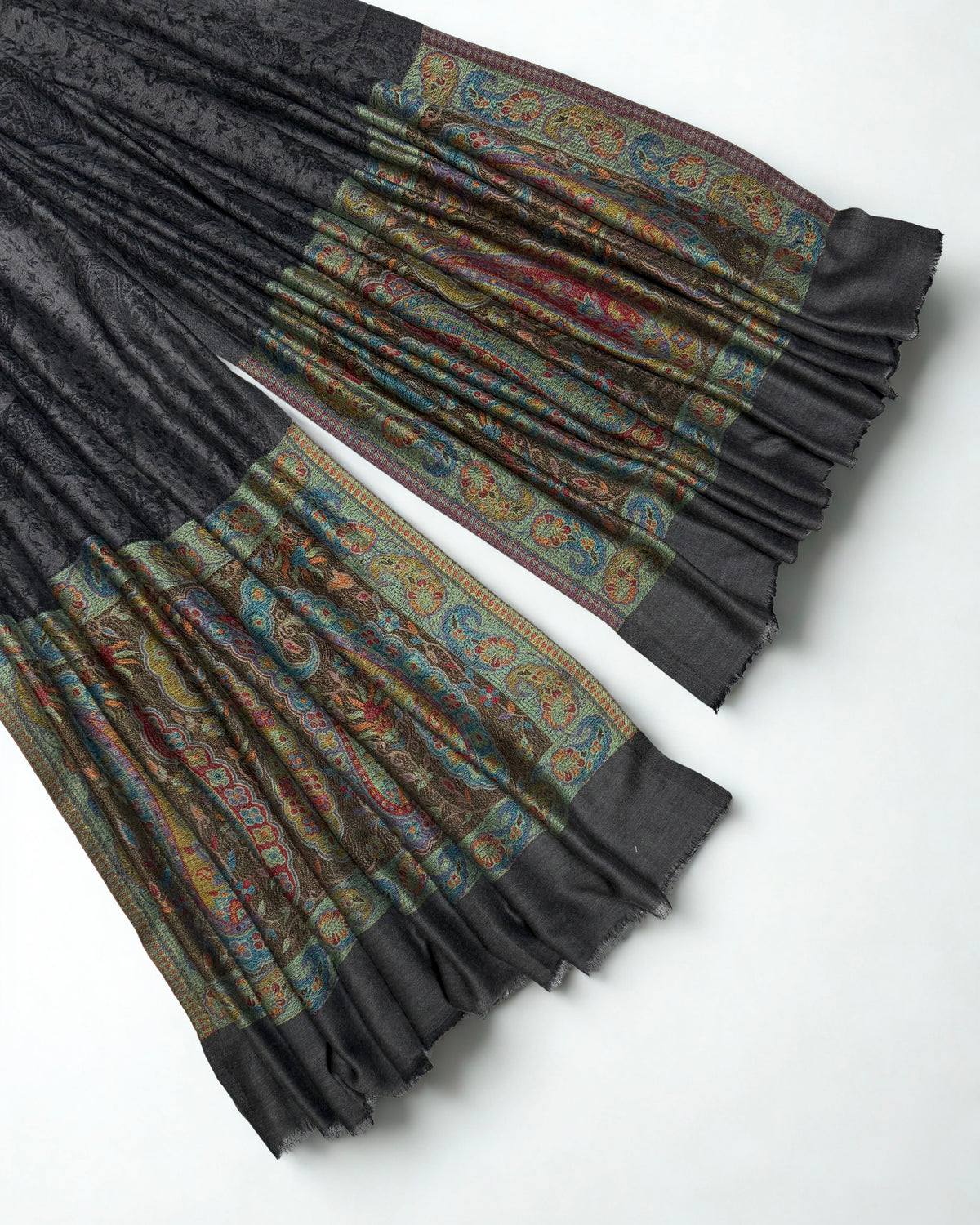 Close-up of both ends of a dark charcoal pashmina ring shawl, showing the teal, crimson, saffron and sage woven paisley pallas