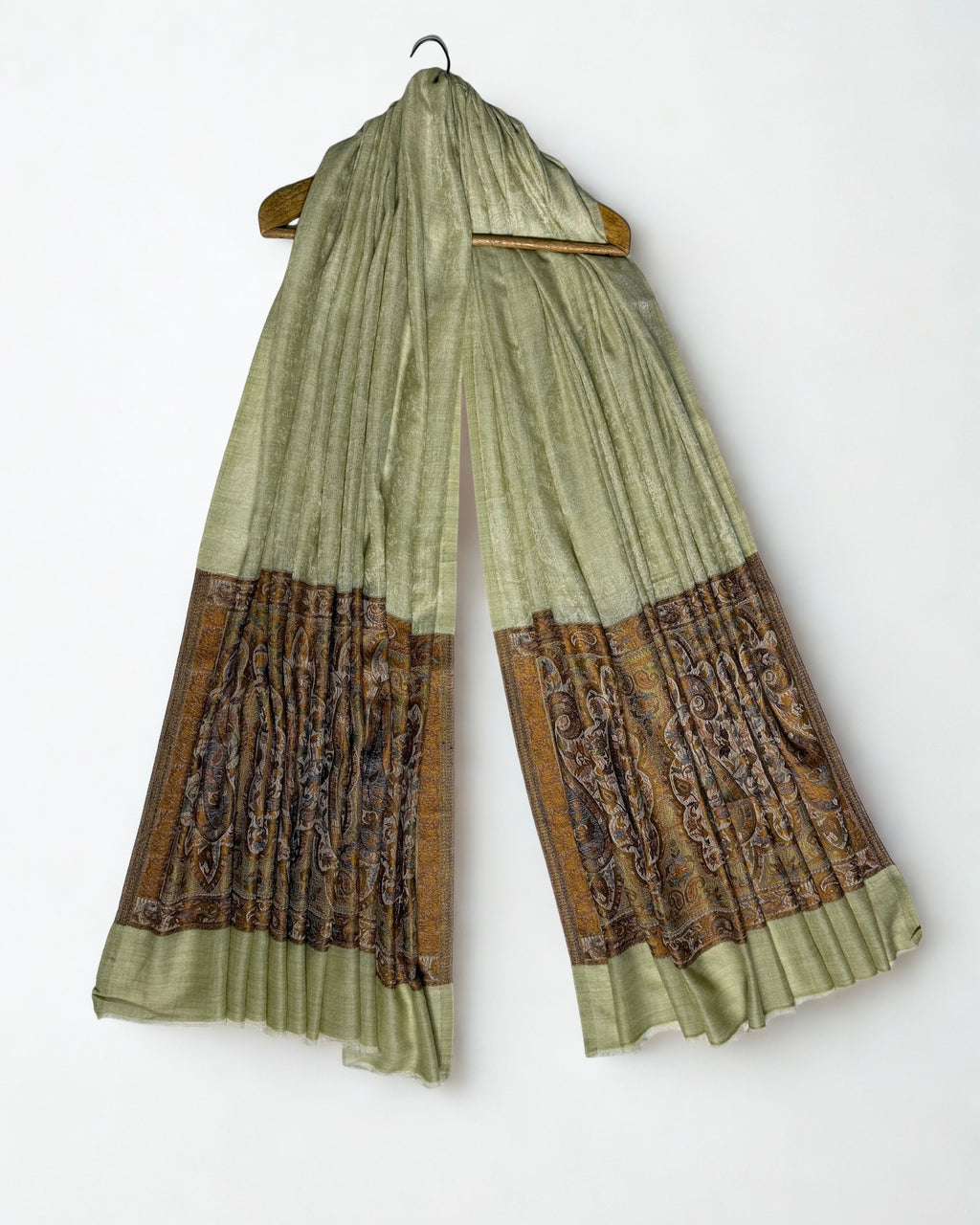 Pistachio pashmina ring shawl hanging from a wooden hanger, pale green field above and bronze paisley pallas at both ends