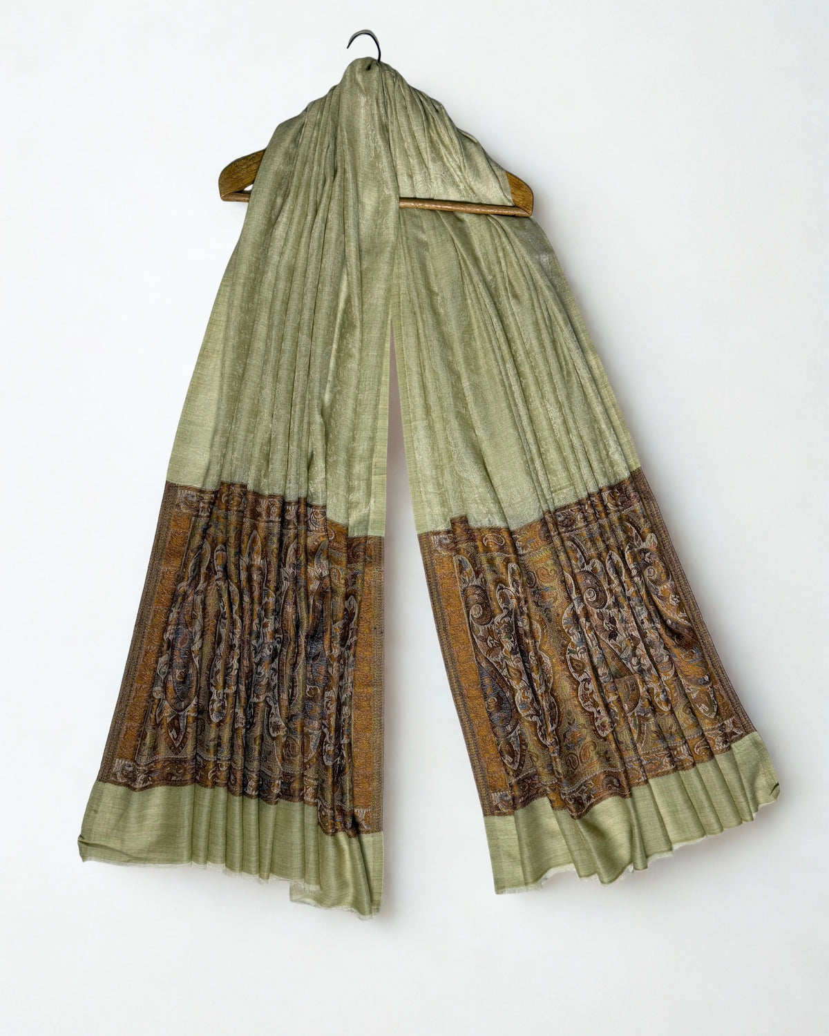 Pistachio pashmina ring shawl hanging from a wooden hanger, pale green field above and bronze paisley pallas at both ends