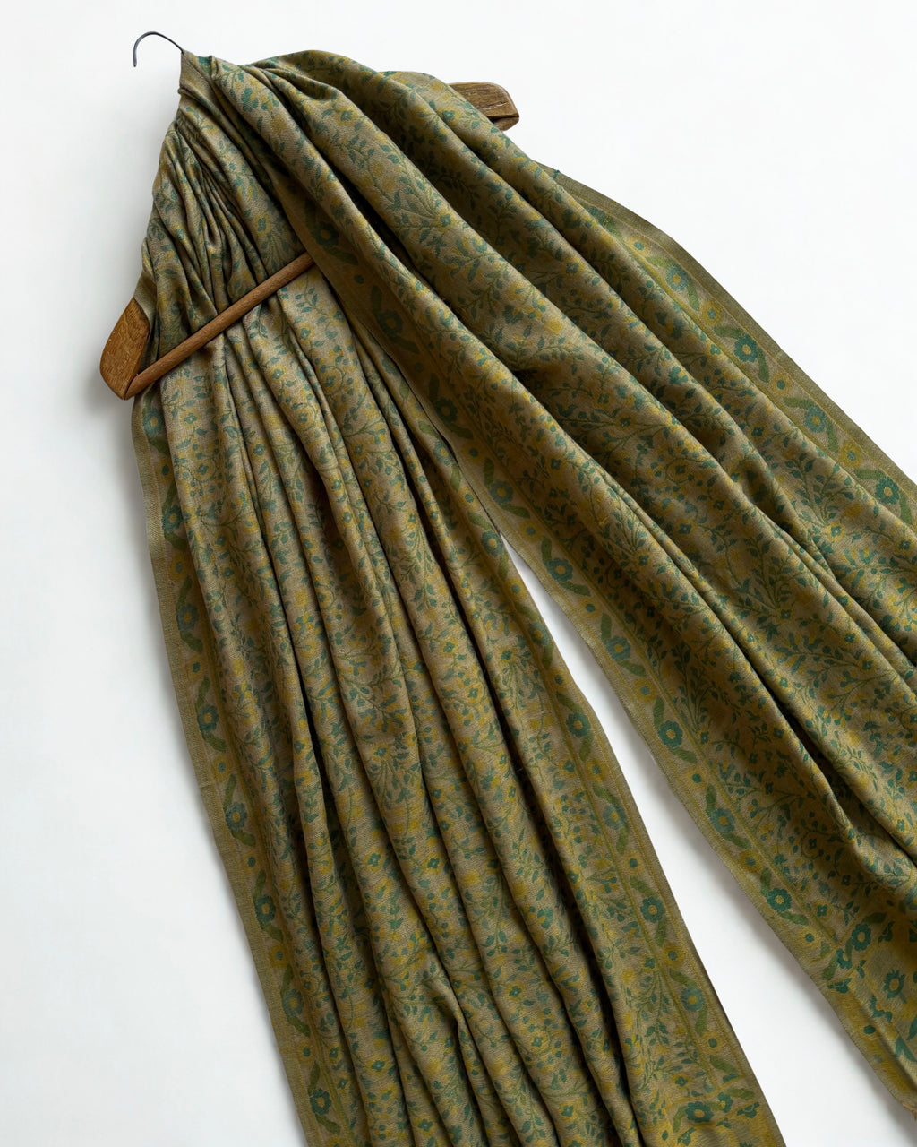 Moss and ochre Kani pashmina shawl draped over a wooden hanger, showing its full length and drape