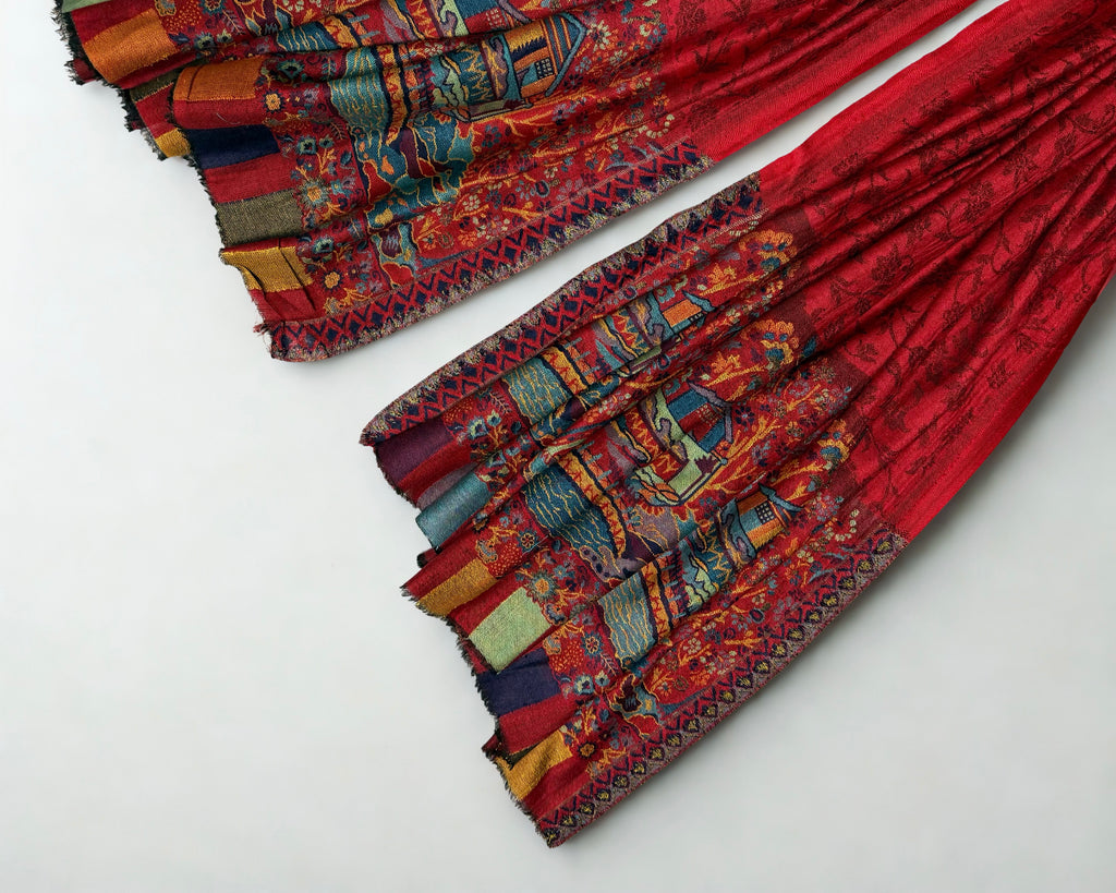 Detail of the woven houses, trees and coloured stripes at the edge of the ruby red Palladar shawl