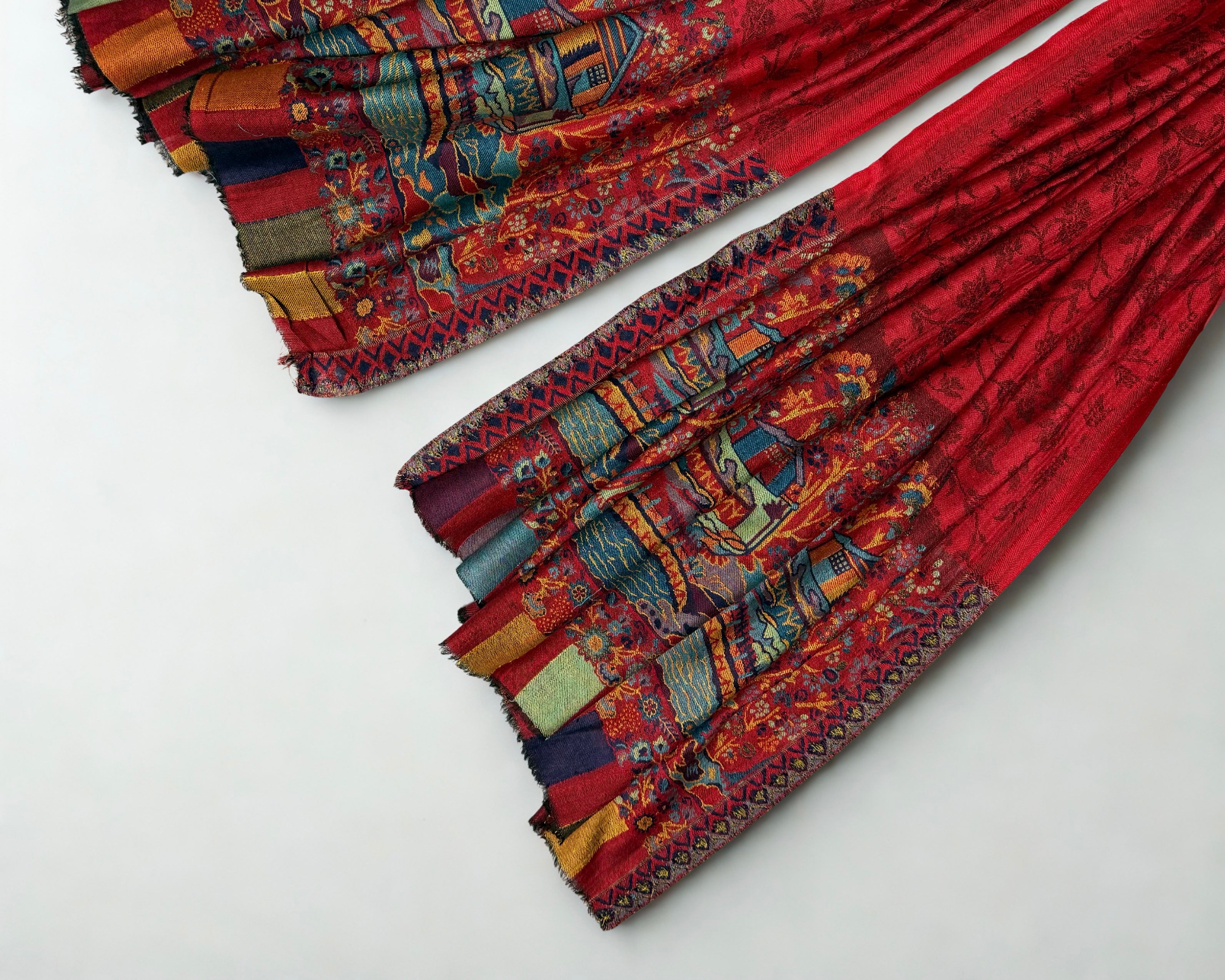 Detail of the woven houses, trees and coloured stripes at the edge of the ruby red Palladar shawl
