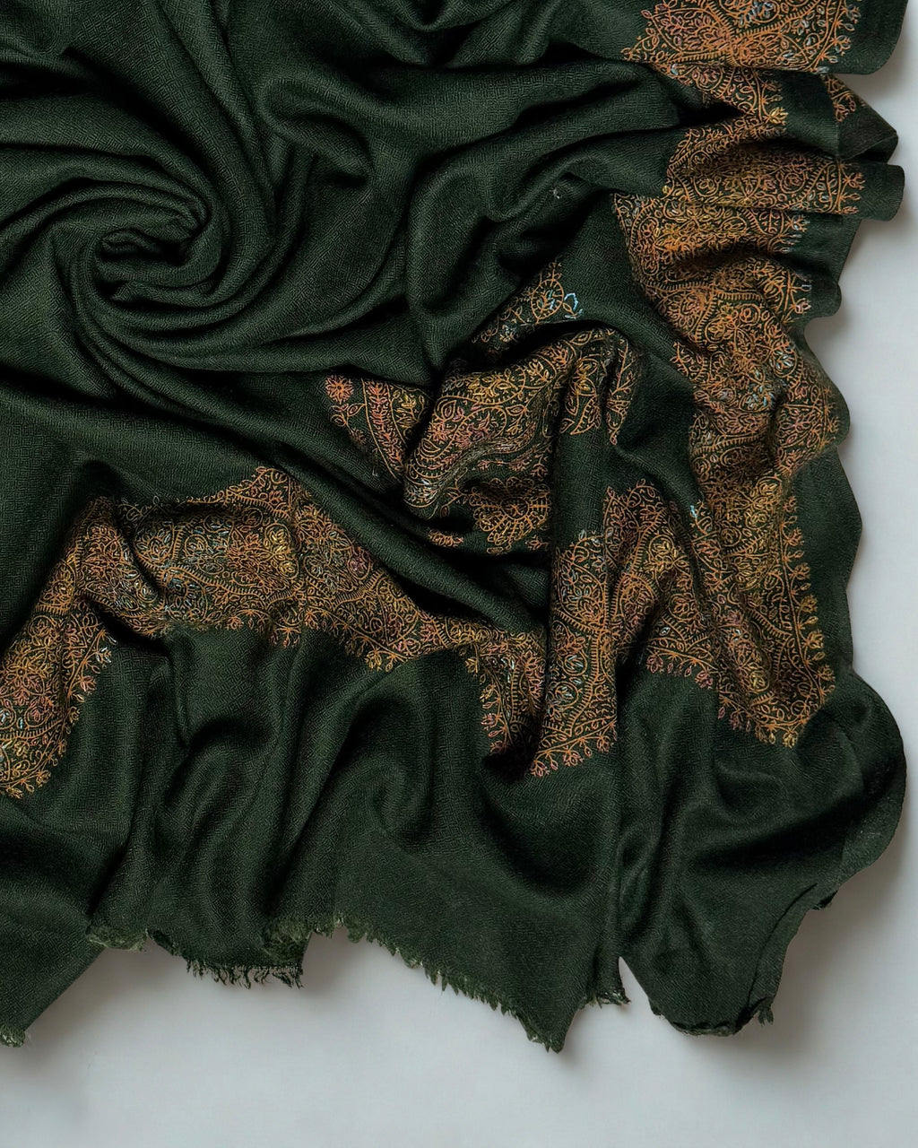 Forest green Swati Shahtoosh shawl draped in soft folds, showing the fine self-coloured lattice in the weave beside the embroidered border