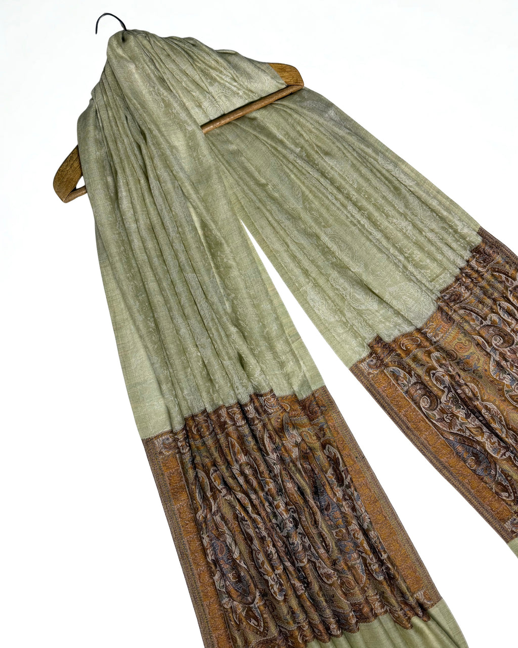 Pistachio fine pashmina ring shawl on a wooden hanger at an angle, with woven bronze pallas at both ends