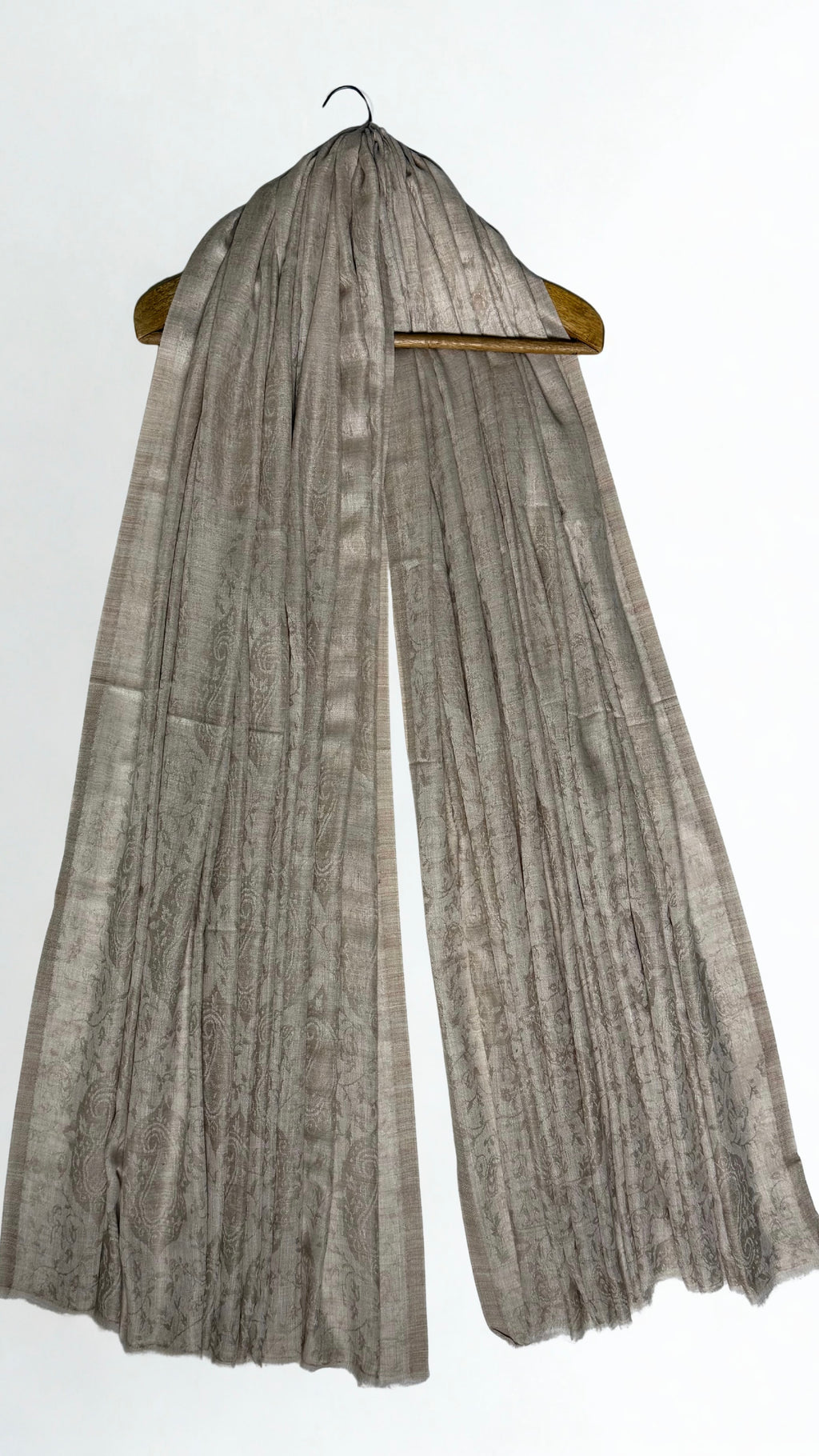 Stone taupe pashmina ring shawl hanging from a wooden hanger, showing the woven paisley and lustrous edge stripes