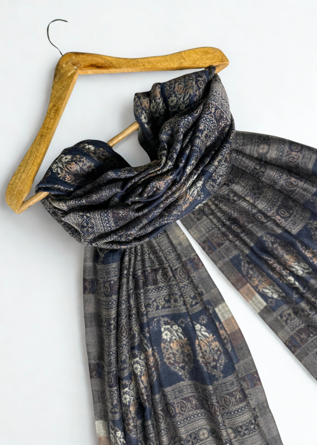 Indigo and bronze Indian pashmina shawl gathered over a hanger, showing the softness of the drape and the banded floral weave