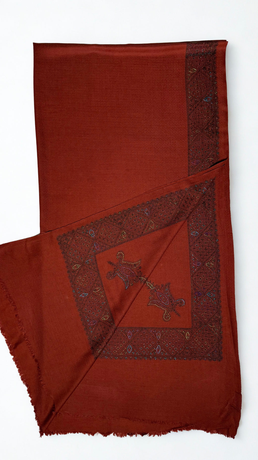 Rust Swati Shahtoosh shawl with one corner turned back, showing the hand-embroidered lattice border meeting at the corner with two paisley buta motifs