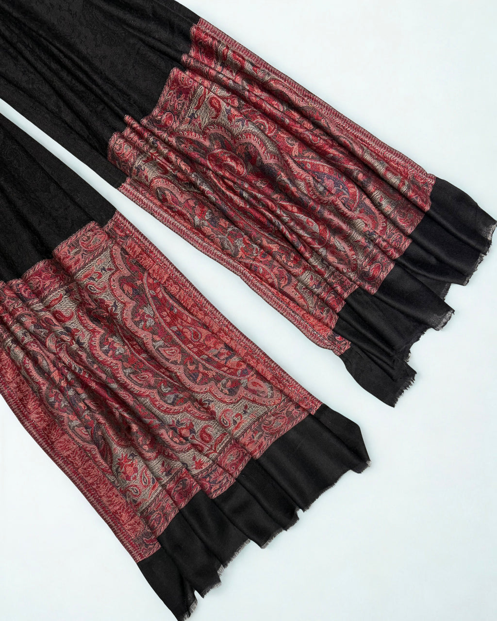 Full length view of a black pashmina ring shawl with a broad crimson and silver paisley end panel