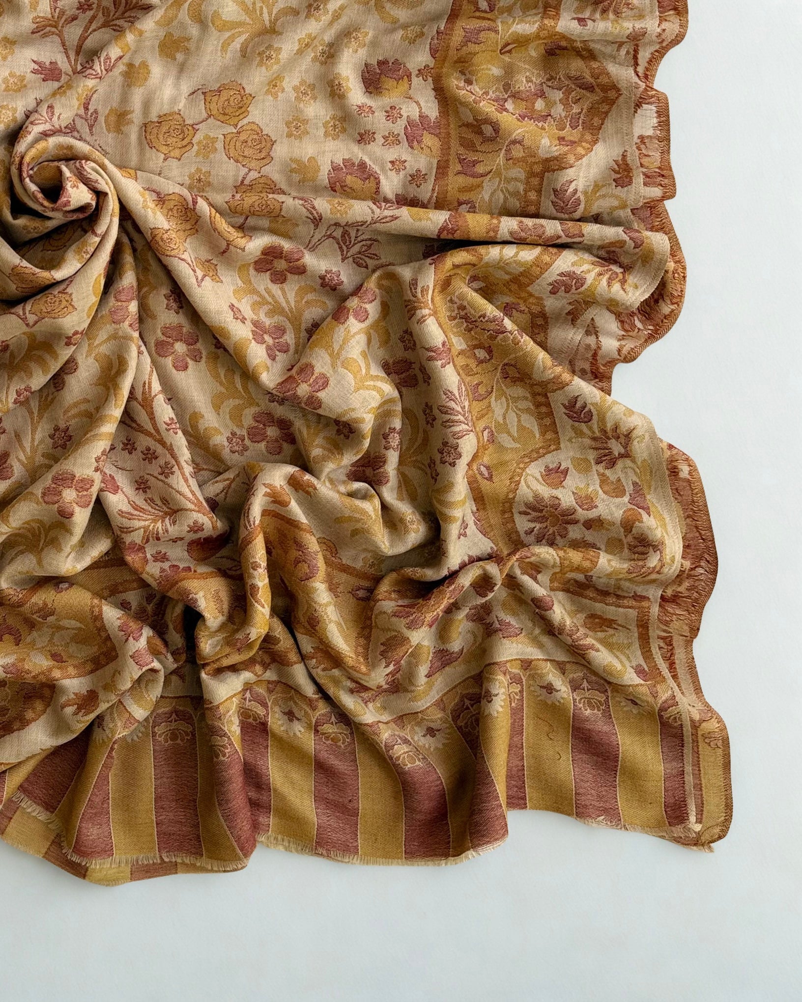 Close view of the rose and ochre flowering sprays woven into a pale sand pashmina ground