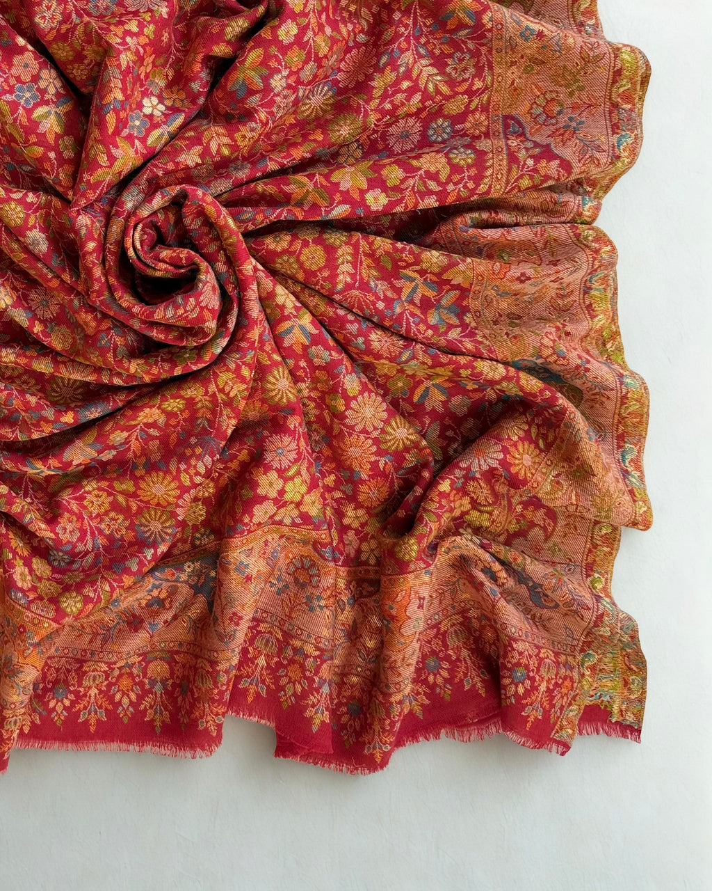 Crimson Zari Kani pashmina shawl gathered in a soft swirl, showing the drape and the gold zari lifting under light