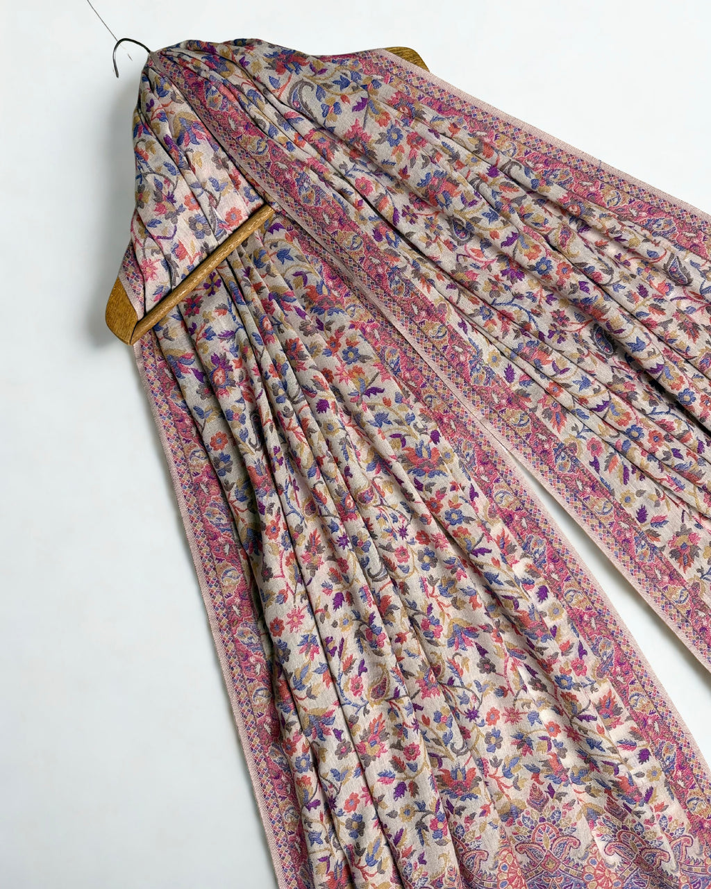Almond and cornflower Kani pashmina shawl laid flat, floral and paisley field with a scalloped medallion border and striped paisley end panel